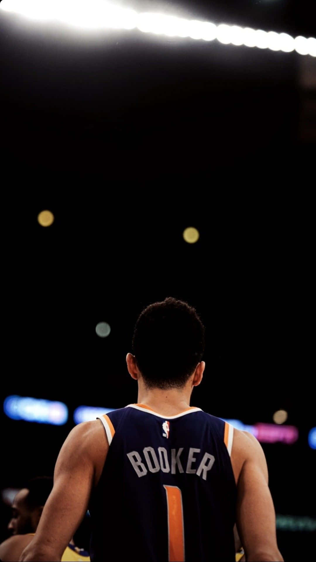 桌布 壁紙 — 一名身穿 'BOOKER 1' 球衣的籃球運動員在明亮的場館燈光下背對鏡頭站立。