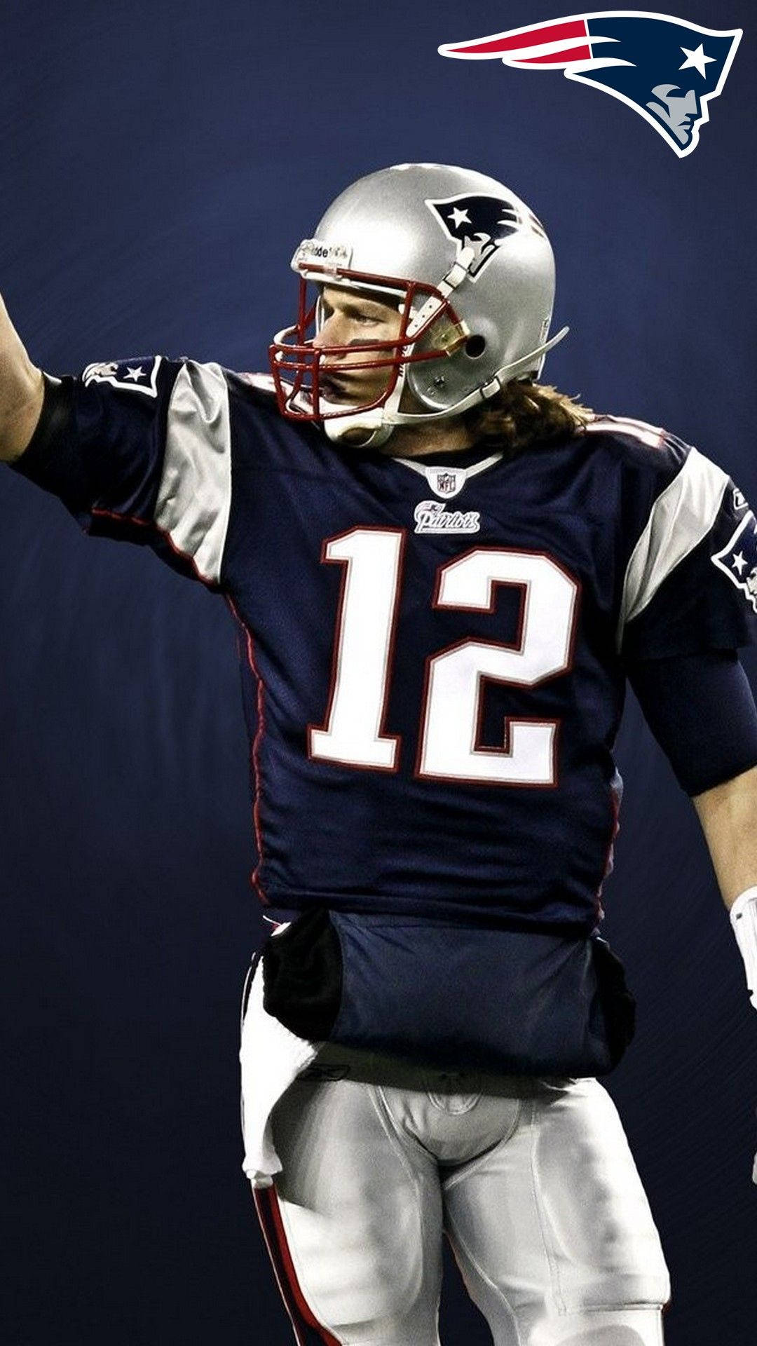 Tom Brady 桌布 壁紙 — 一名身穿12號球衣的新英格蘭愛國者隊美式足球員在深藍色背景的體育場聚光燈下舉起手臂。