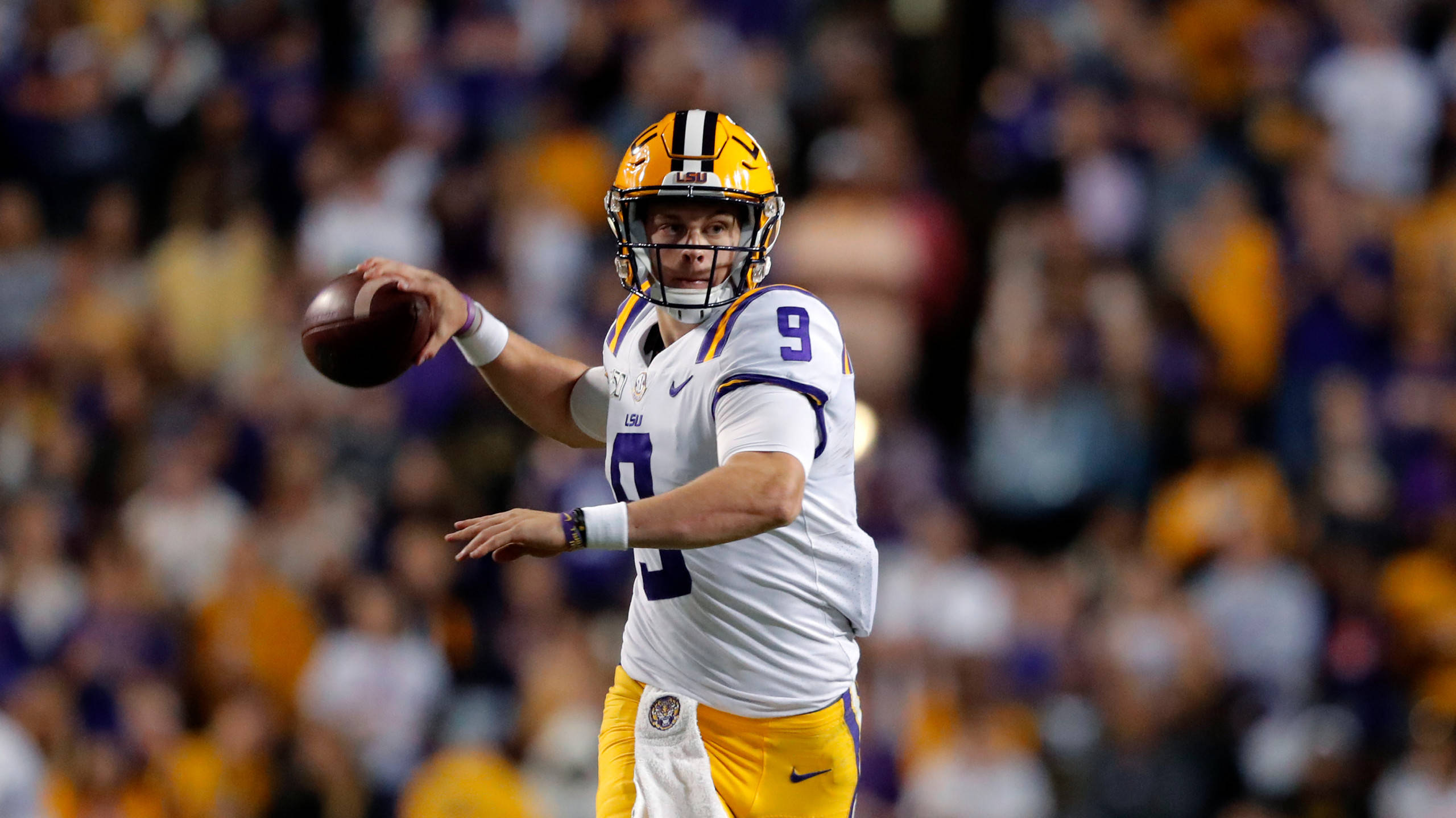 Joe Burrow 桌布 壁紙 — 一名身穿LSU制服的美式足球四分衛在球場燈光下準備投球，背景有模糊的球迷。