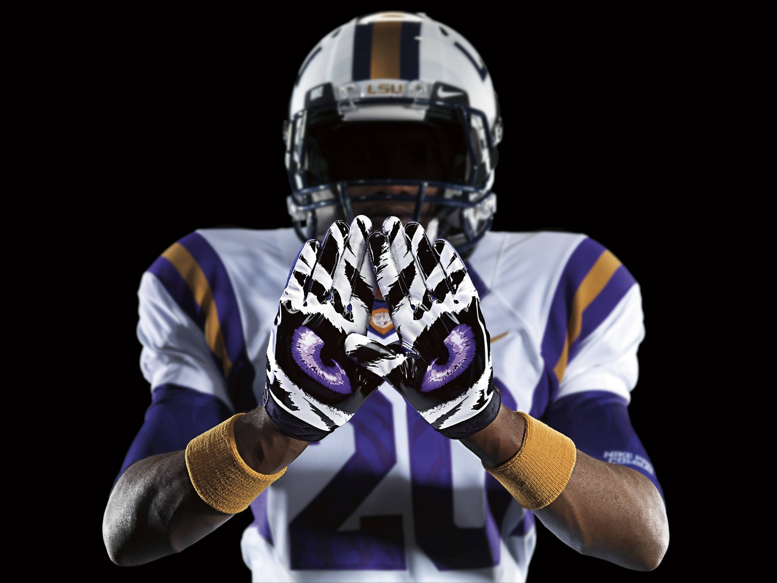 Lsu 桌布 壁紙 — 一名身穿LSU裝備的美式足球員在黑色背景前舉起帶有紫色虎眼設計的手套。