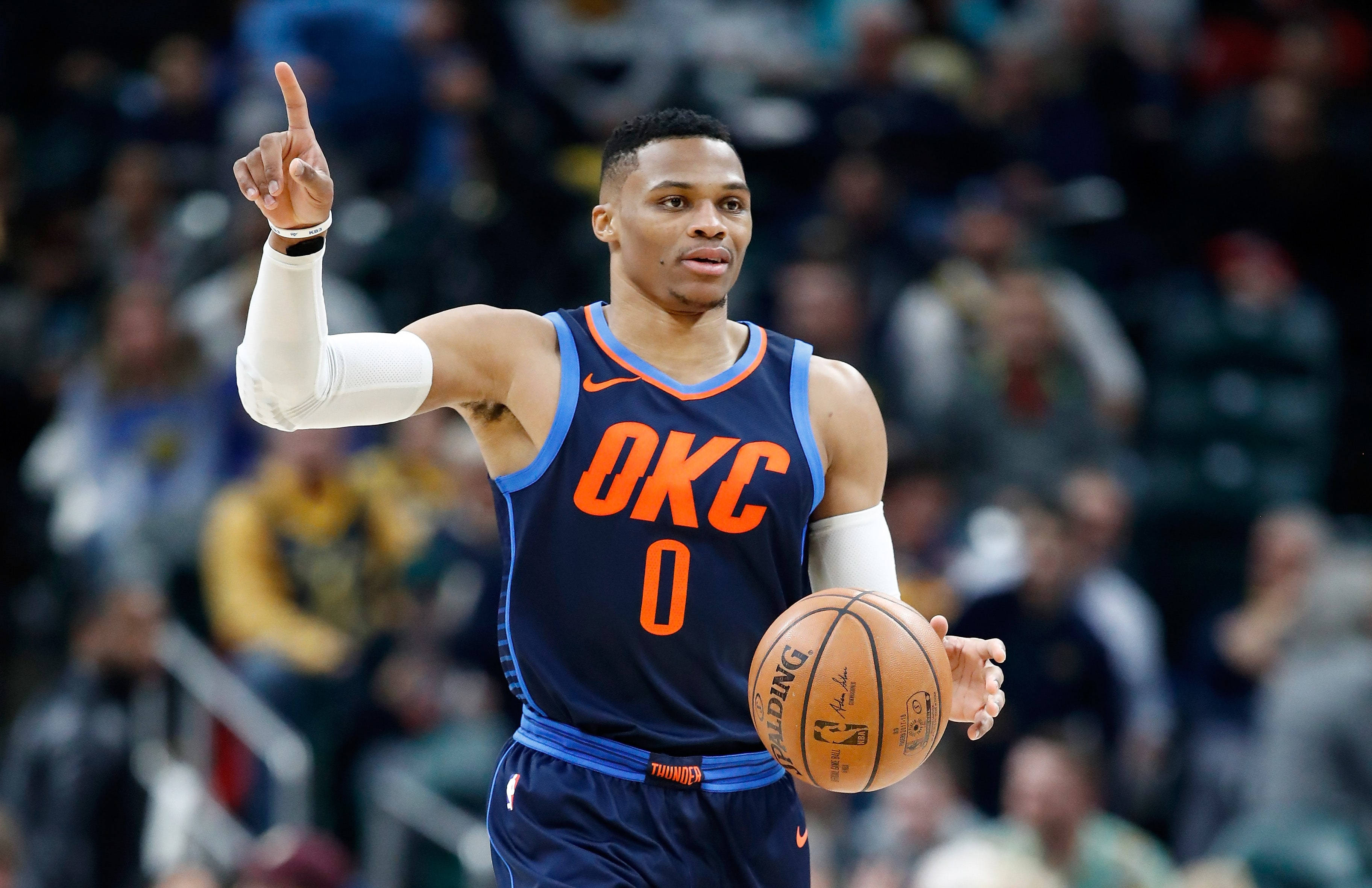 Westbrook 桌布 壁紙 — 一名身穿OKC球衣的籃球運動員在比賽中拿著球並向上指，背景有模糊的觀眾。