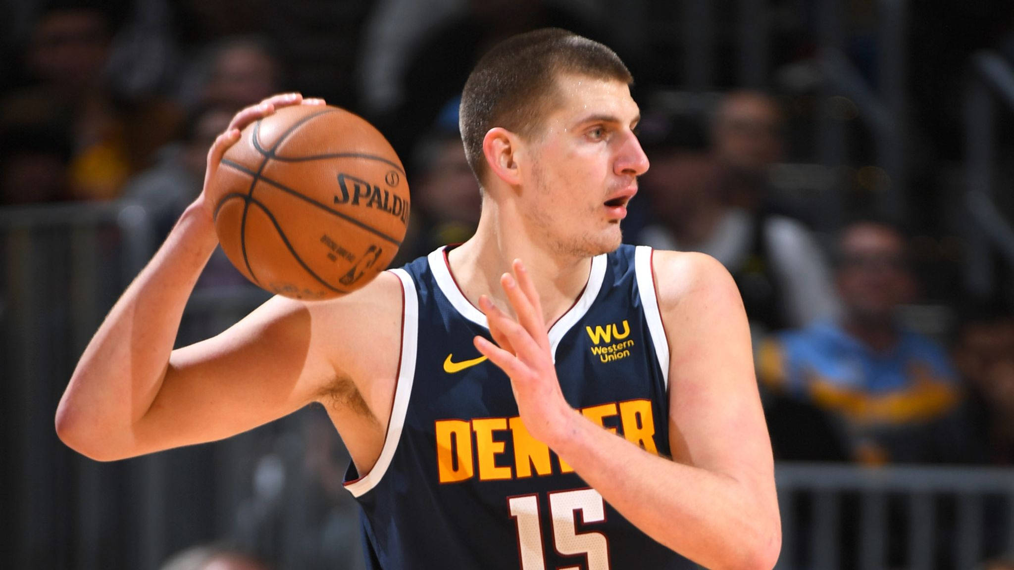 Jokic 桌布 壁紙 — 一名身穿丹佛球衣的籃球運動員在明亮的場館燈光下，於一場激烈的比賽中準備投擲斯伯丁籃球。