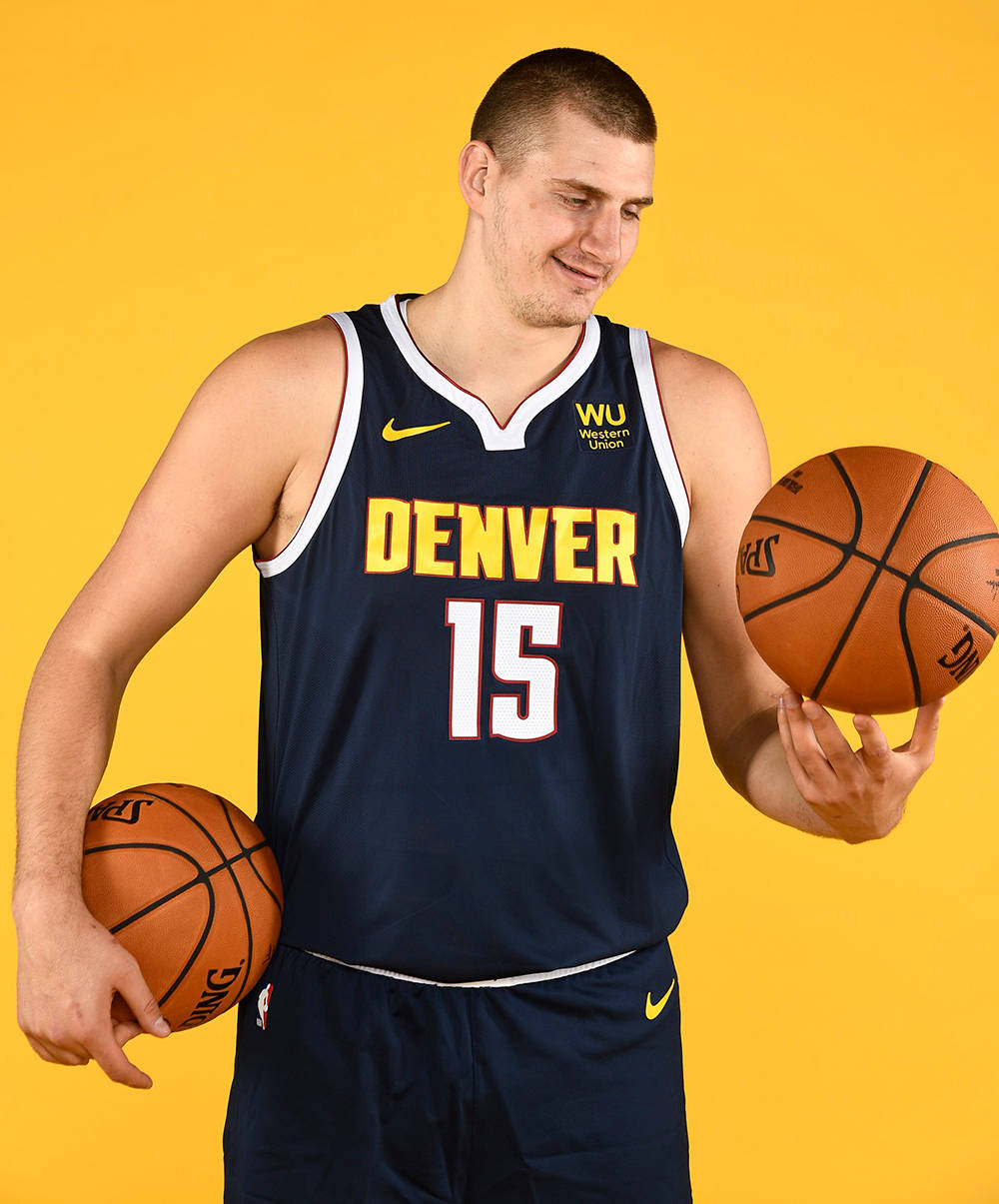 Jokic 桌布 壁紙 — 一名身穿丹佛金塊球衣的籃球運動員，在純黃色背景前手持兩個籃球。