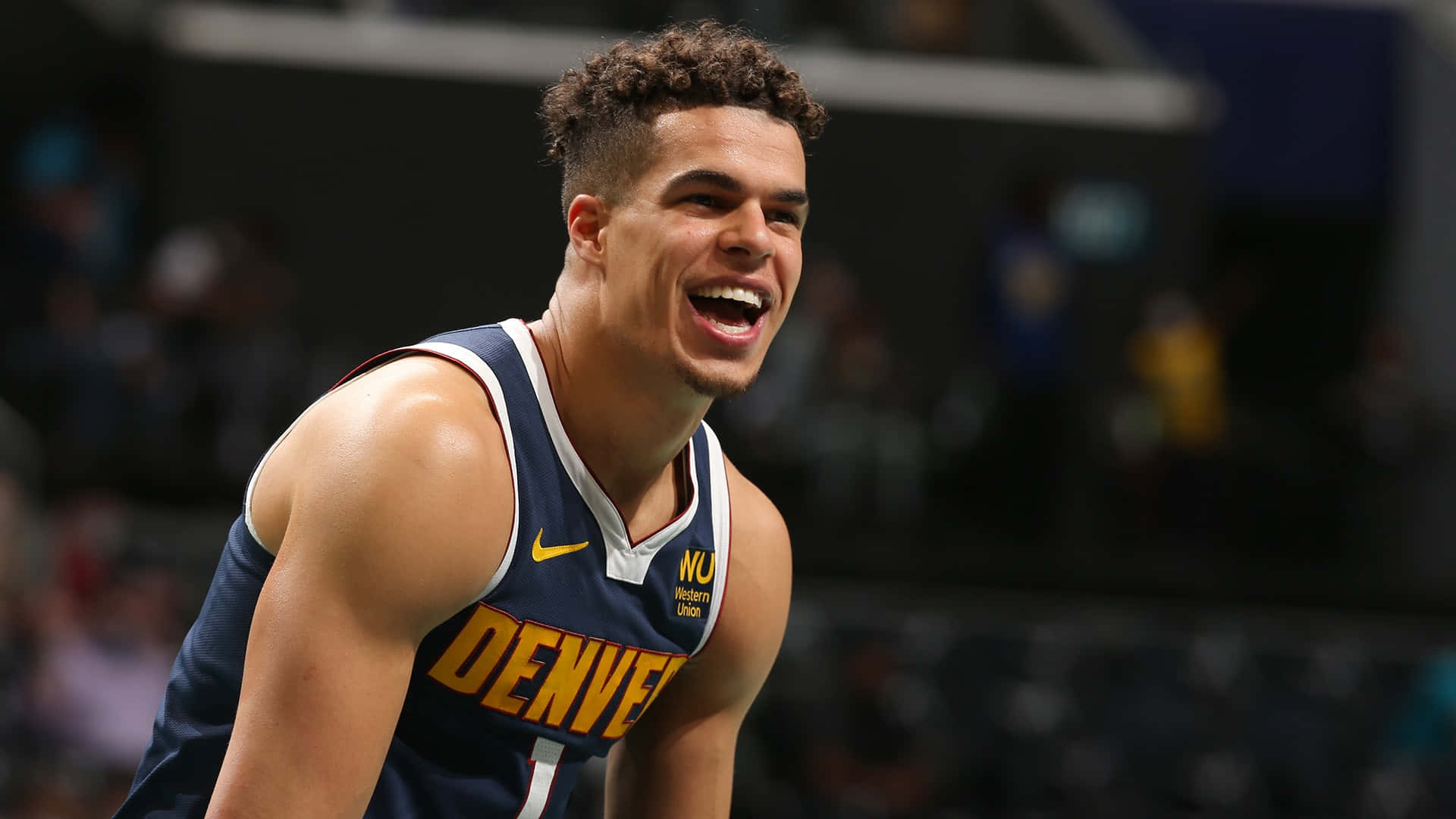 NBA 桌布 壁紙 — 一名身穿丹佛金塊隊球衣的籃球運動員在球場燈光下比賽時開懷大笑。