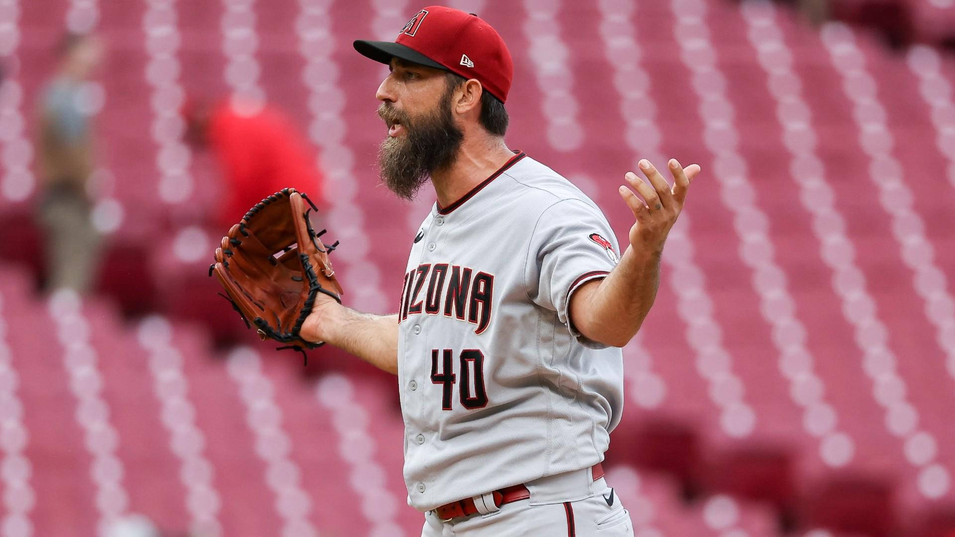 madison bumgarner 桌布 壁紙 — 一名身穿亞利桑那隊制服、留鬍鬚的棒球投手在球場上生動地做手勢，身後是空無一人的紅色體育場座位。