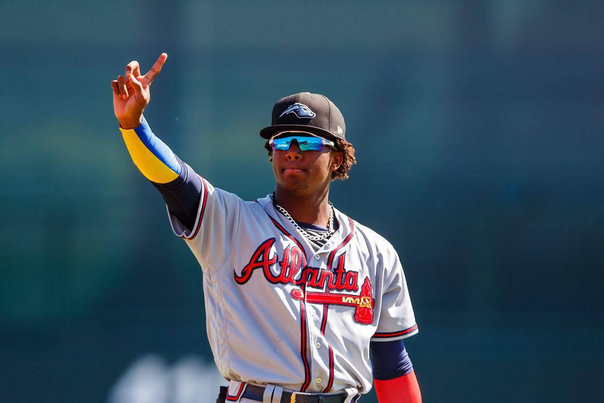 Acuna 桌布 壁紙 — 一名身穿亞特蘭大勇士隊球衣的棒球選手，戴著太陽眼鏡和帽子，比出和平手勢揮手。