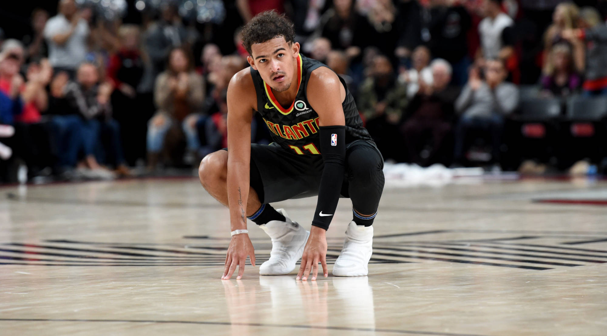 Trae Young 桌布 壁紙 — 一名身穿亞特蘭大球衣的籃球運動員在比賽中跪在球場上，雙手放在地上，背後是模糊的人群。