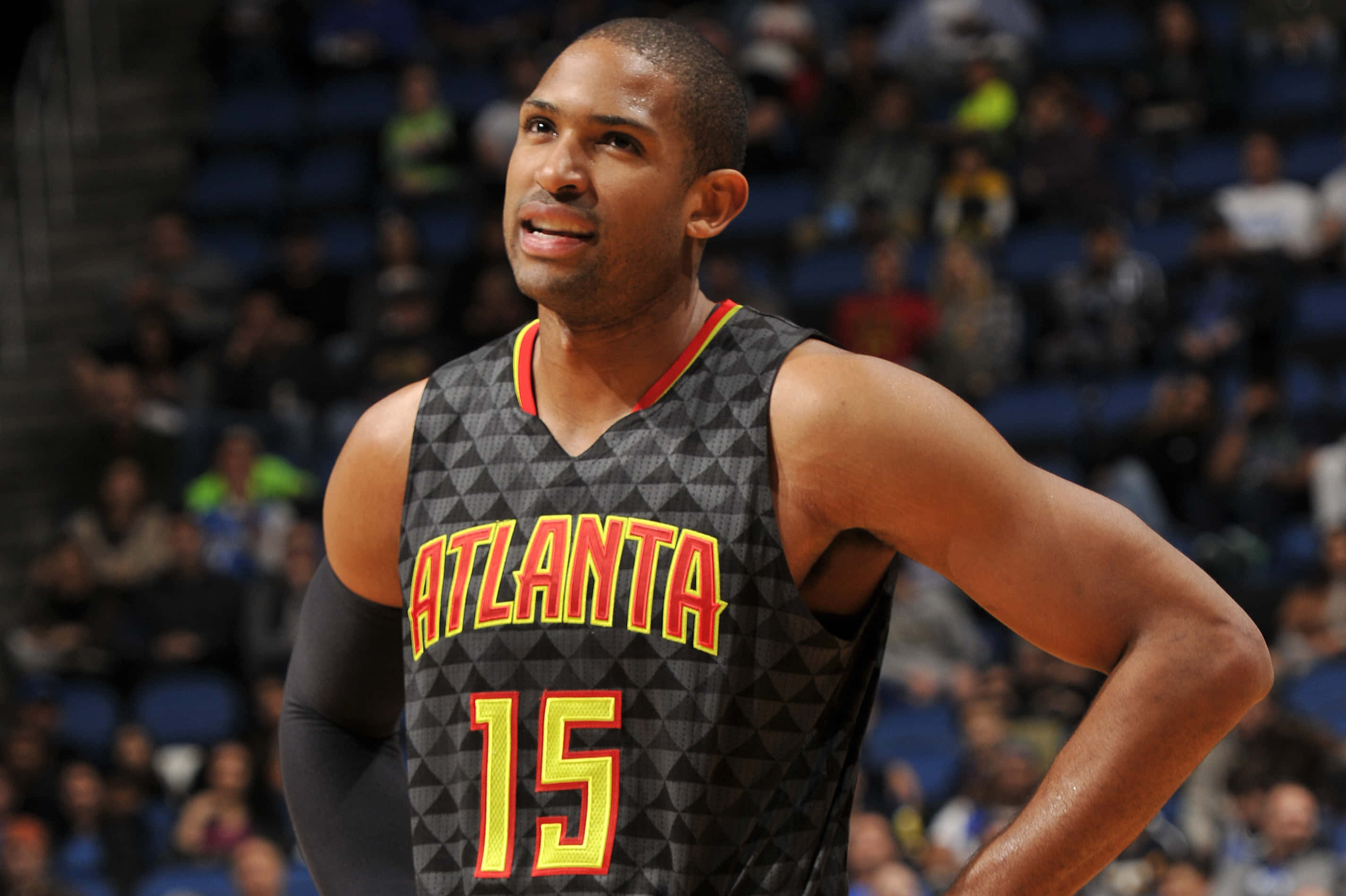 Al Horford 桌布 壁紙 — 一名身穿亞特蘭大球衣的籃球運動員在比賽中雙手叉腰，自信地站在場館燈光下。
