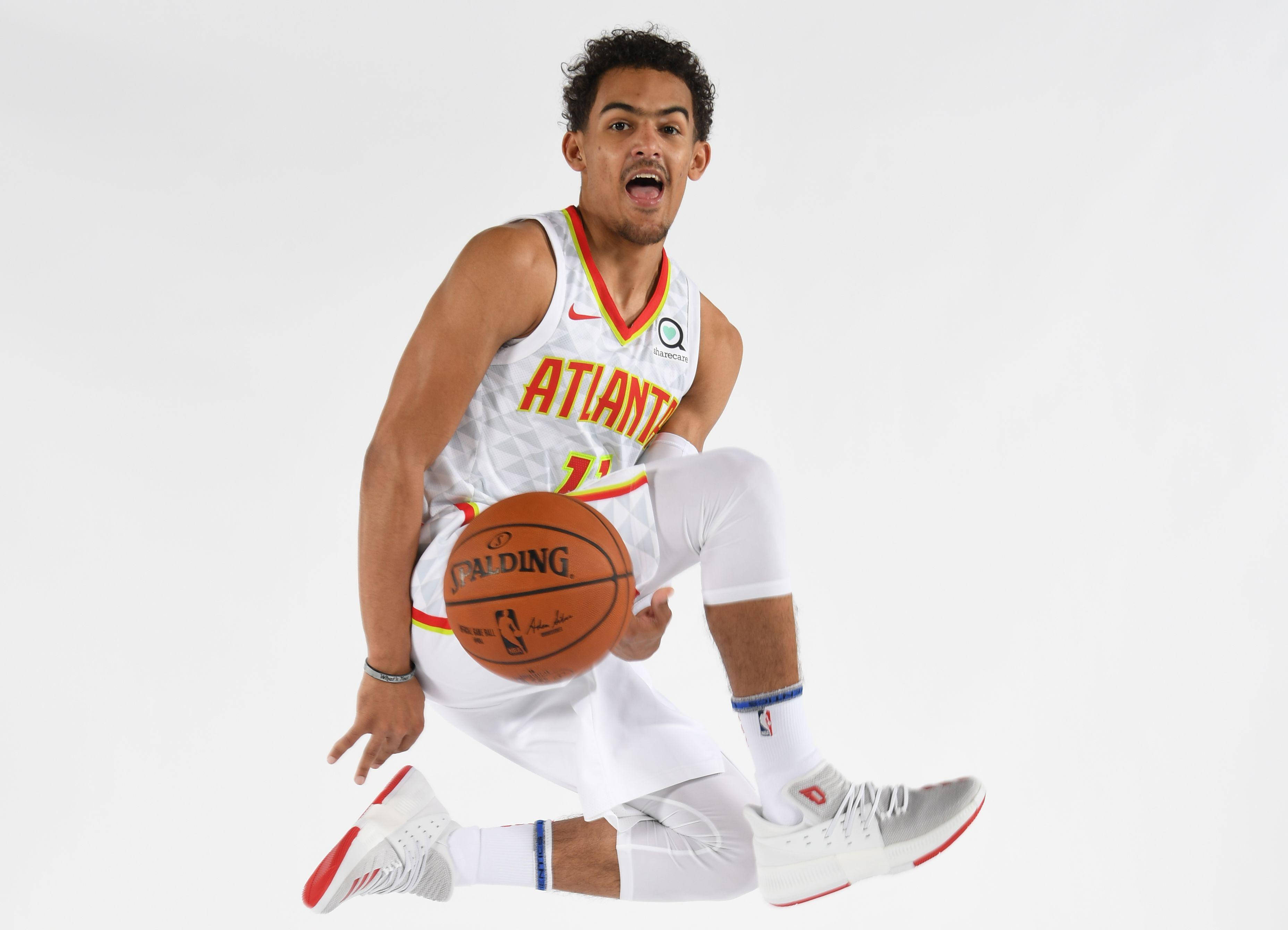 Trae Young 桌布 壁紙 — 一名身穿亞特蘭大老鷹隊球衣的籃球運動員在半空中蹲下，手持籃球，背景為純白色。