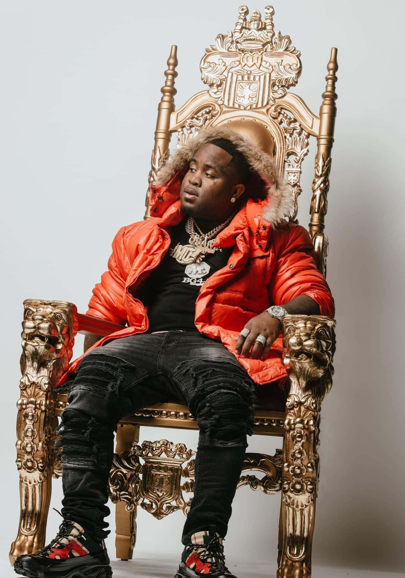 Rappers 桌布 壁紙 — 一名身穿亮橙色羽絨外套的男子，在純白色背景前，威嚴地坐在華麗的金色寶座上。