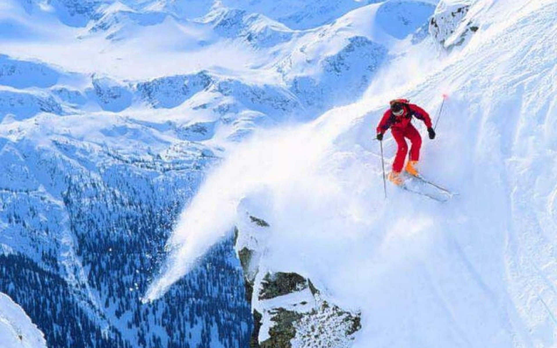 Winter Sports 桌布 壁紙 — 一名身穿亮紅色滑雪服的滑雪者，在陡峭的雪山斜坡上刻滑，揚起一陣粉雪。