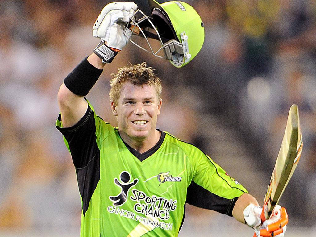 Warner 桌布 壁紙 — 一名身穿亮綠色球衣的板球運動員在夜間高舉頭盔，手持球棒，勝利歡呼。