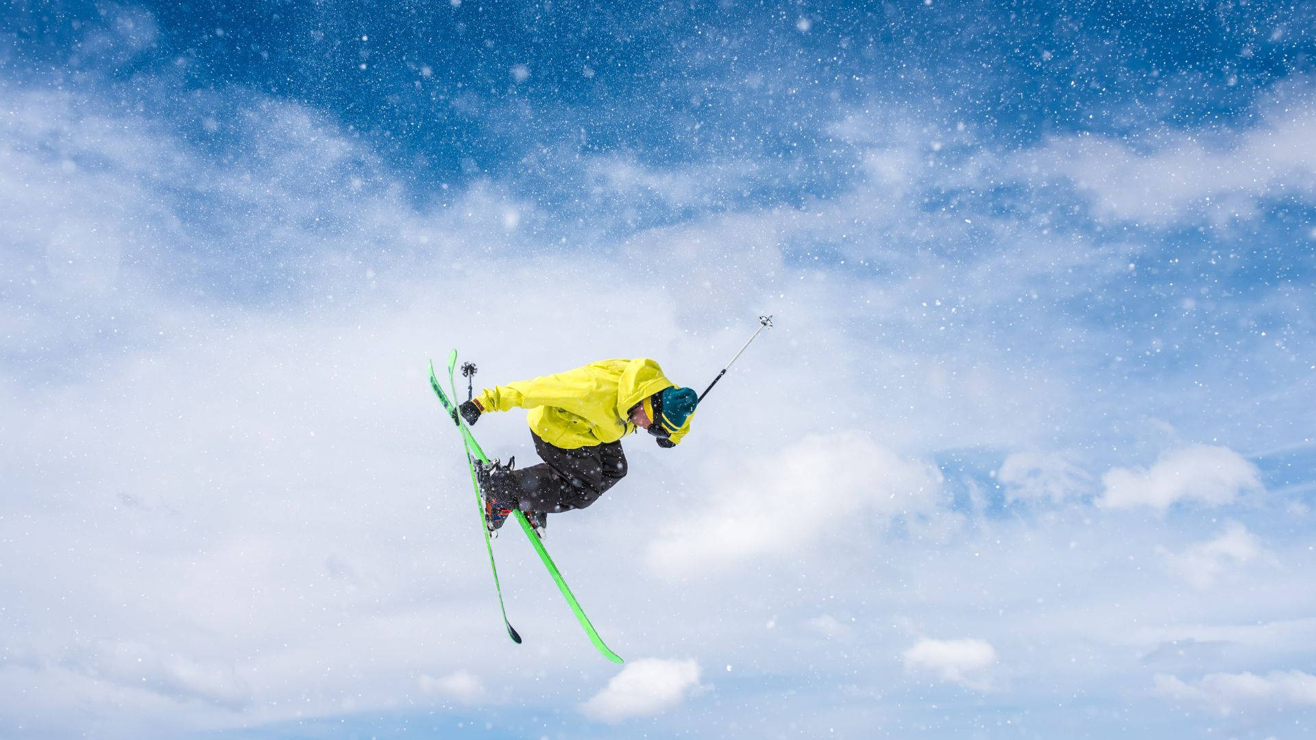 冬天 桌布 壁紙 — 一名身穿亮黃色夾克的滑雪運動員在白雪皚皚的空氣中翱翔，背景是湛藍的天空和蓬鬆的雲朵。