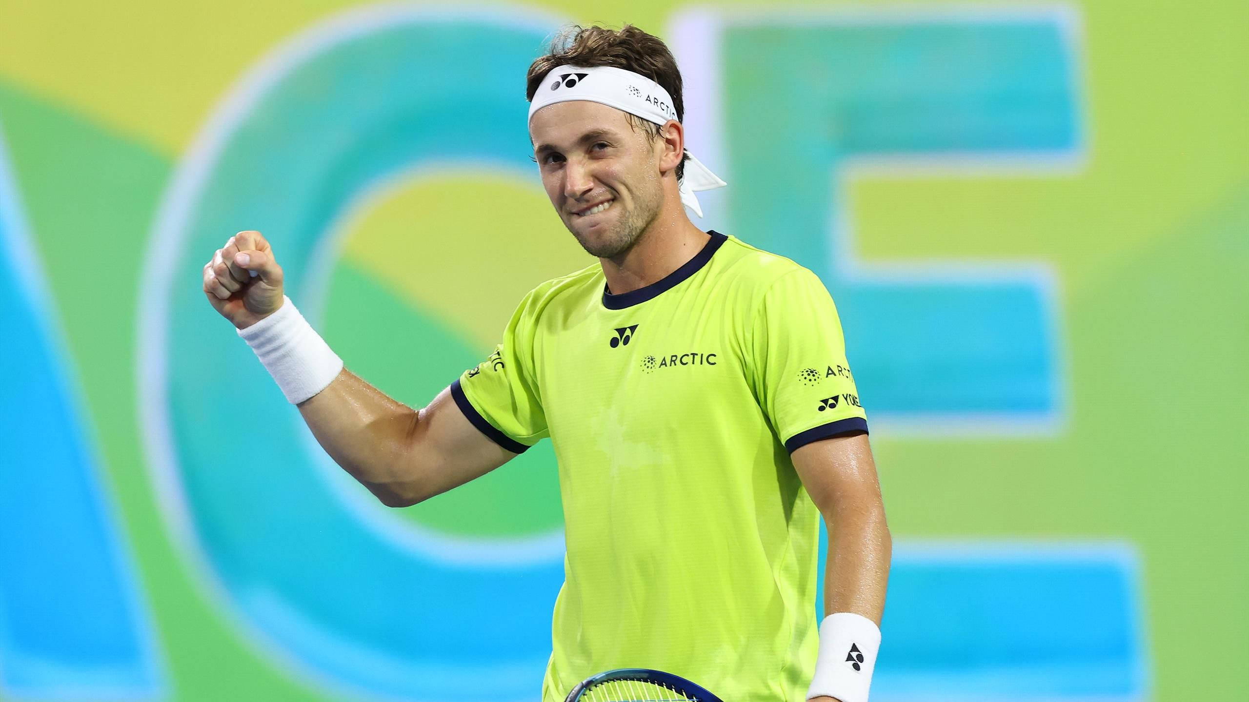 Tennis 桌布 壁紙 — 一名身穿亮黃色球衣的男網球運動員在色彩繽紛的球場上握拳慶祝。