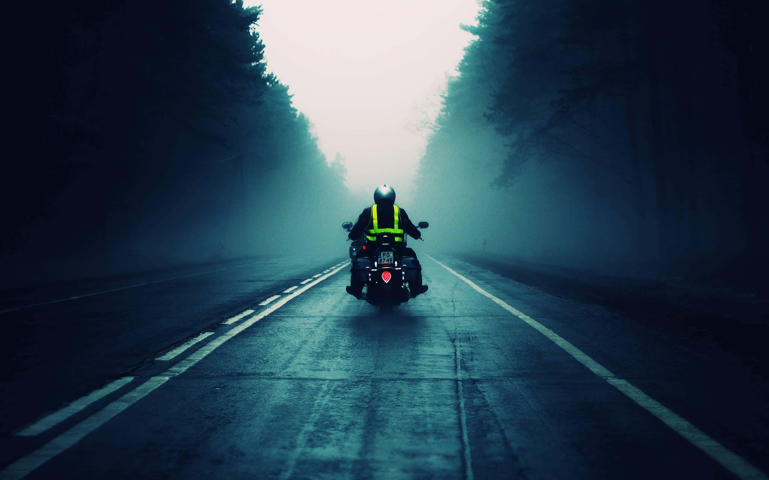 Road 桌布 壁紙 — 一名身穿亮黃色背心的孤獨摩托車手在朦朧的天空下，沿著霧氣瀰漫的森林道路駛離。