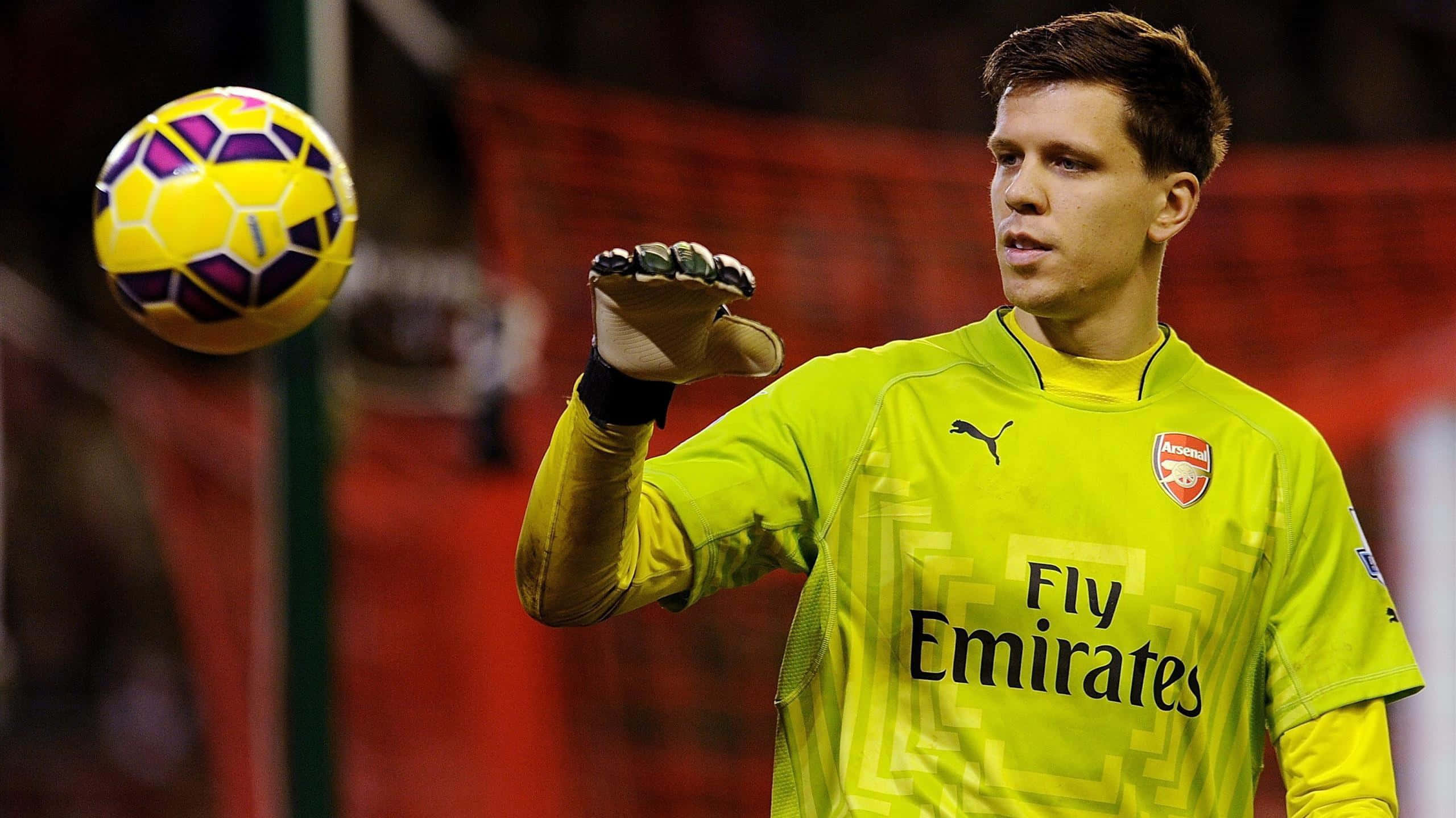 Wojciech Szczesny 桌布 壁紙 — 一名身穿亮黃色阿森納球衣的足球守門員準備接住一個鮮黃色和紫色的球。