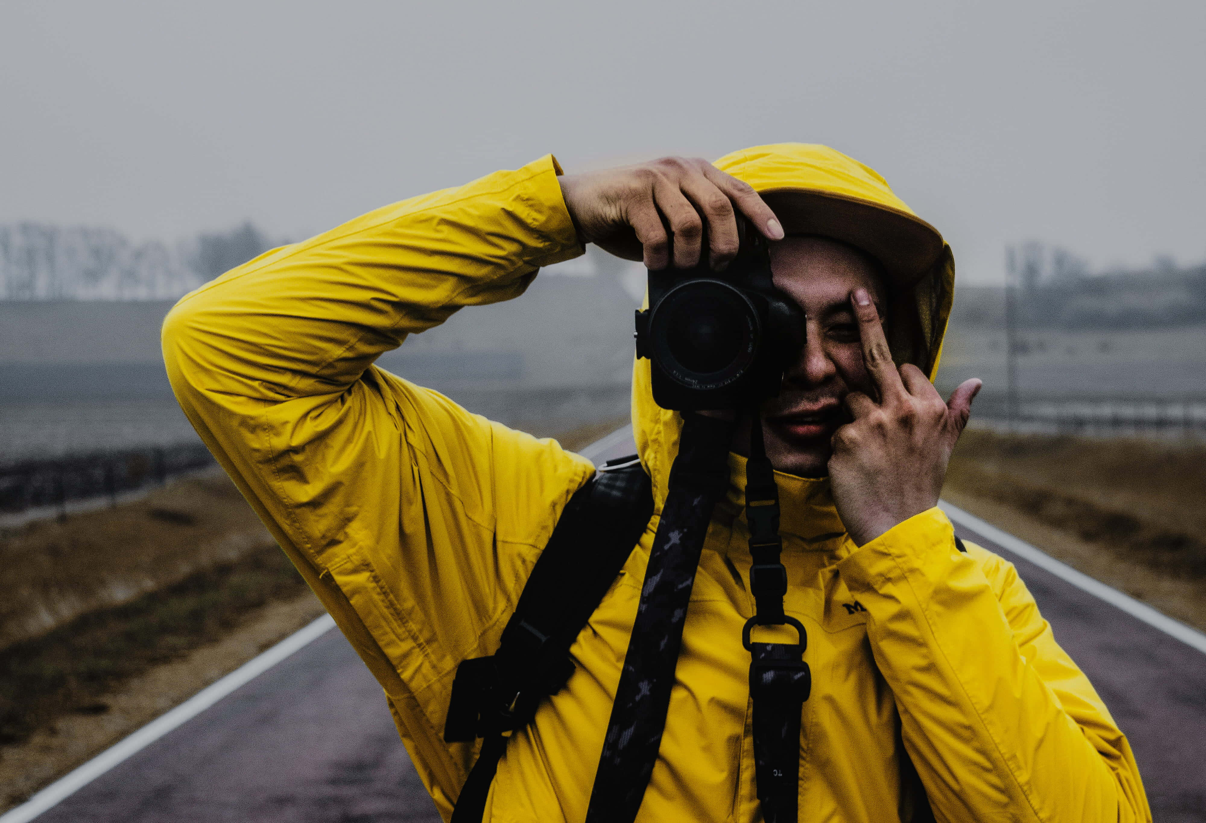 rude 桌布 壁紙 — 一名身穿亮黃色雨衣的人，在霧氣瀰漫的路邊將相機舉到臉前，同時做出和平手勢。