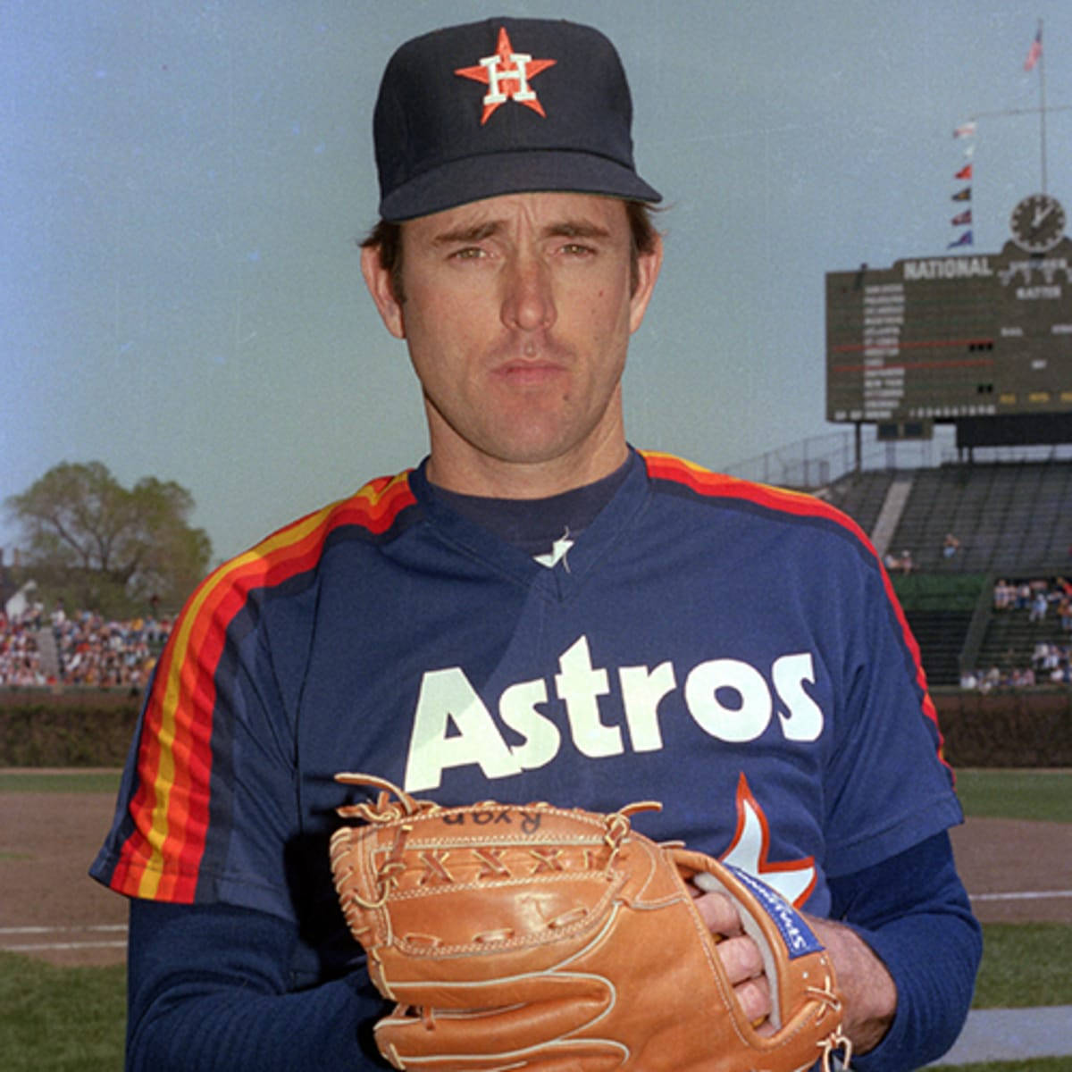 Nolan Ryan 桌布 壁紙 — 一名身穿休士頓太空人隊球衣的棒球運動員在陽光明媚的球場上拿著手套，身後是體育場座位和記分板。