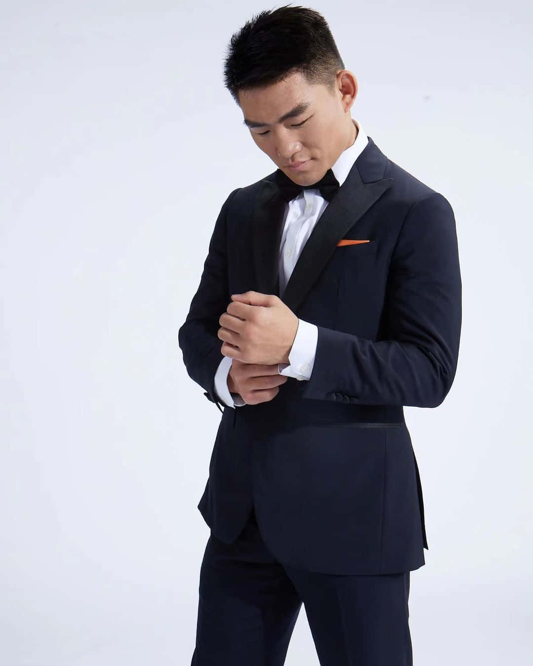 Mens Fashion 桌布 壁紙 — 一名身穿俐落海軍藍燕尾服、搭配橙色袋巾的男子，在純白背景前調整他的袖扣。
