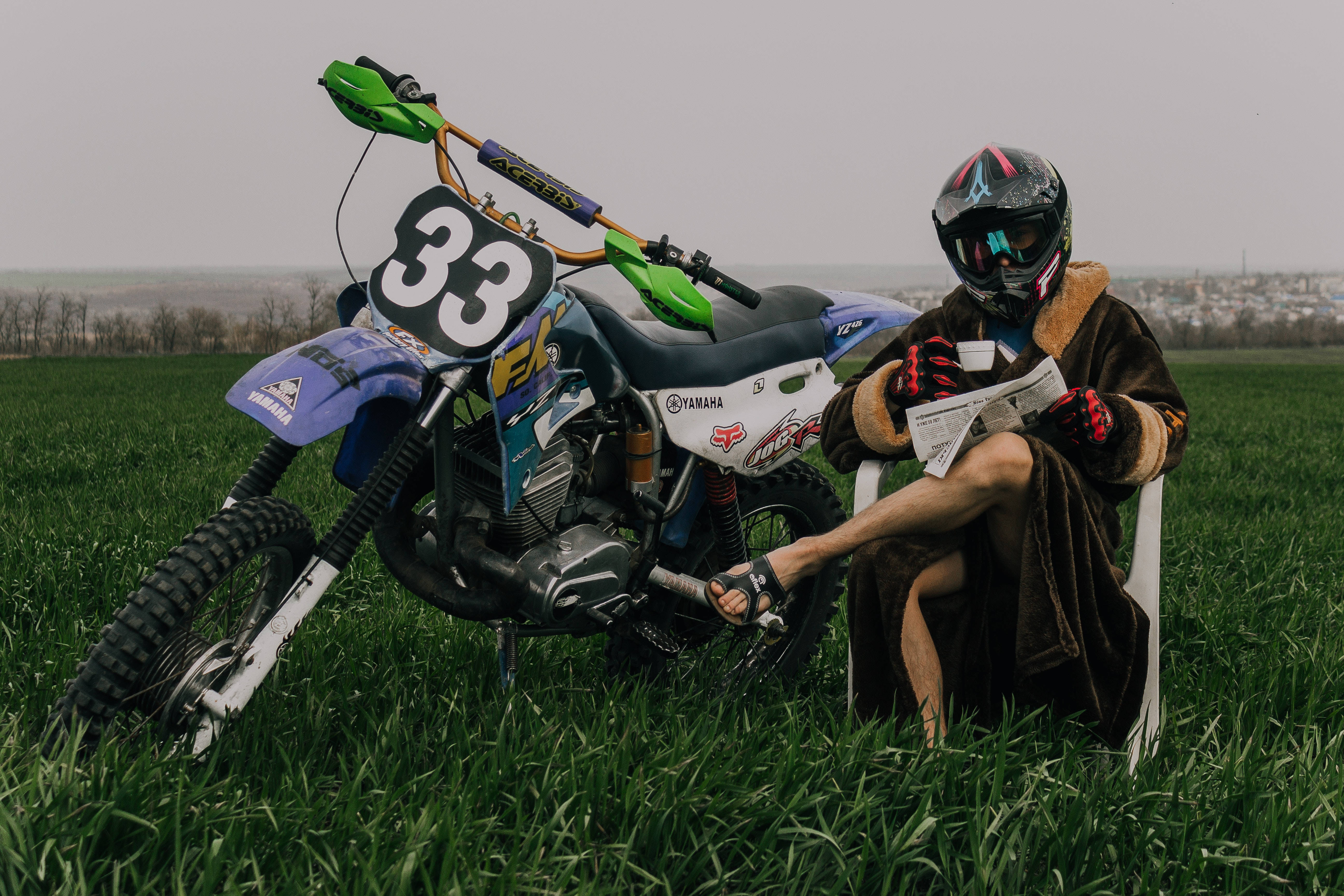 Motocross 桌布 壁紙 — 一名身穿全套裝備的越野摩托車手在田野中放鬆，閱讀報紙，旁邊是他們的33號Yamaha摩托車。