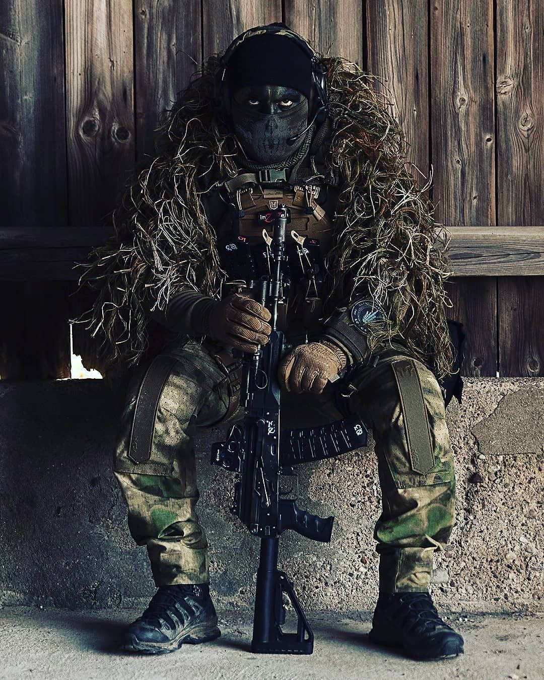 一名迷彩士兵手持步槍靠在木牆上。 — 軍隊 壁紙