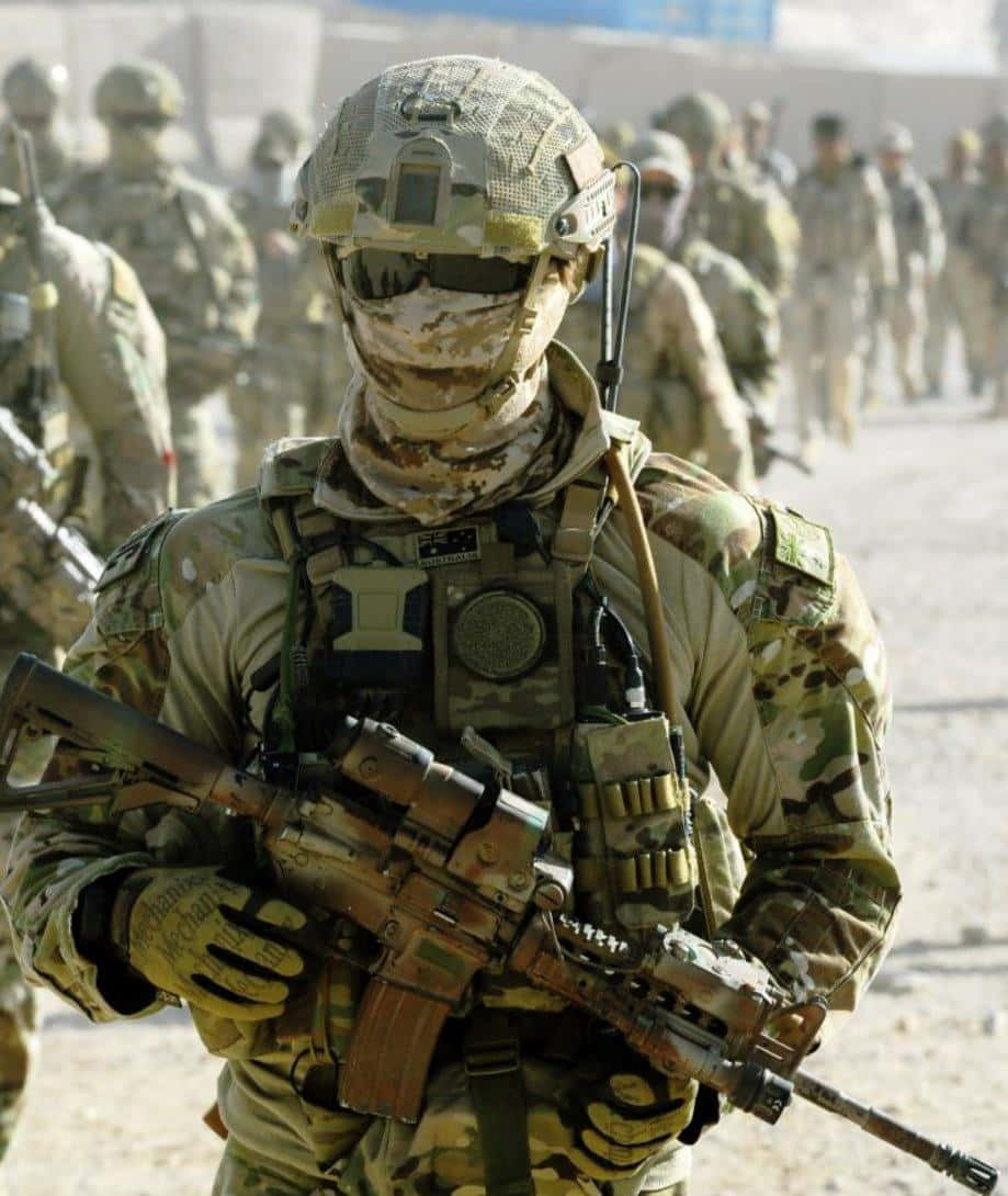 Special Forces 桌布 壁紙 — 一名身穿全套迷彩裝備和頭盔的士兵在塵土飛揚的沙漠軍事環境中警覺地持步槍站立。