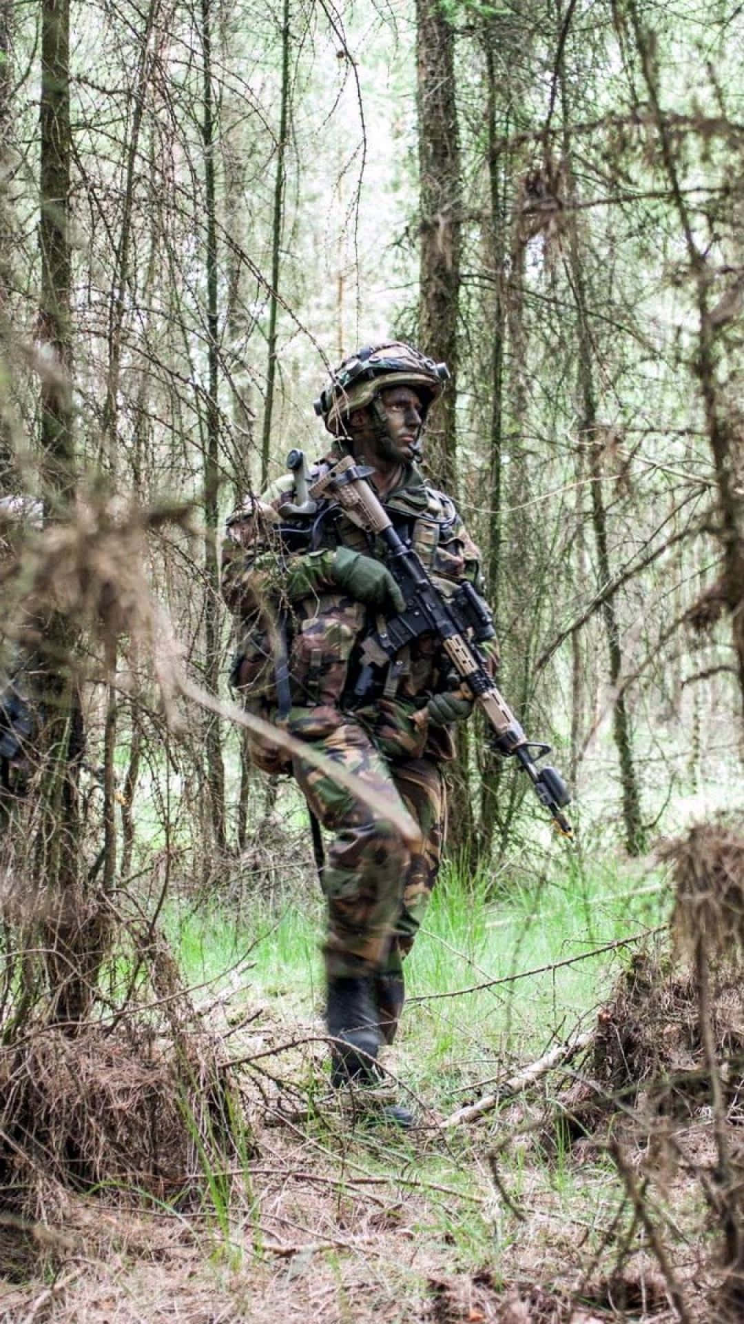 軍事動圖 桌布 壁紙 — 一名身穿全套迷彩裝備的士兵走過一片茂密的森林，樹木高大，灌木叢生。
