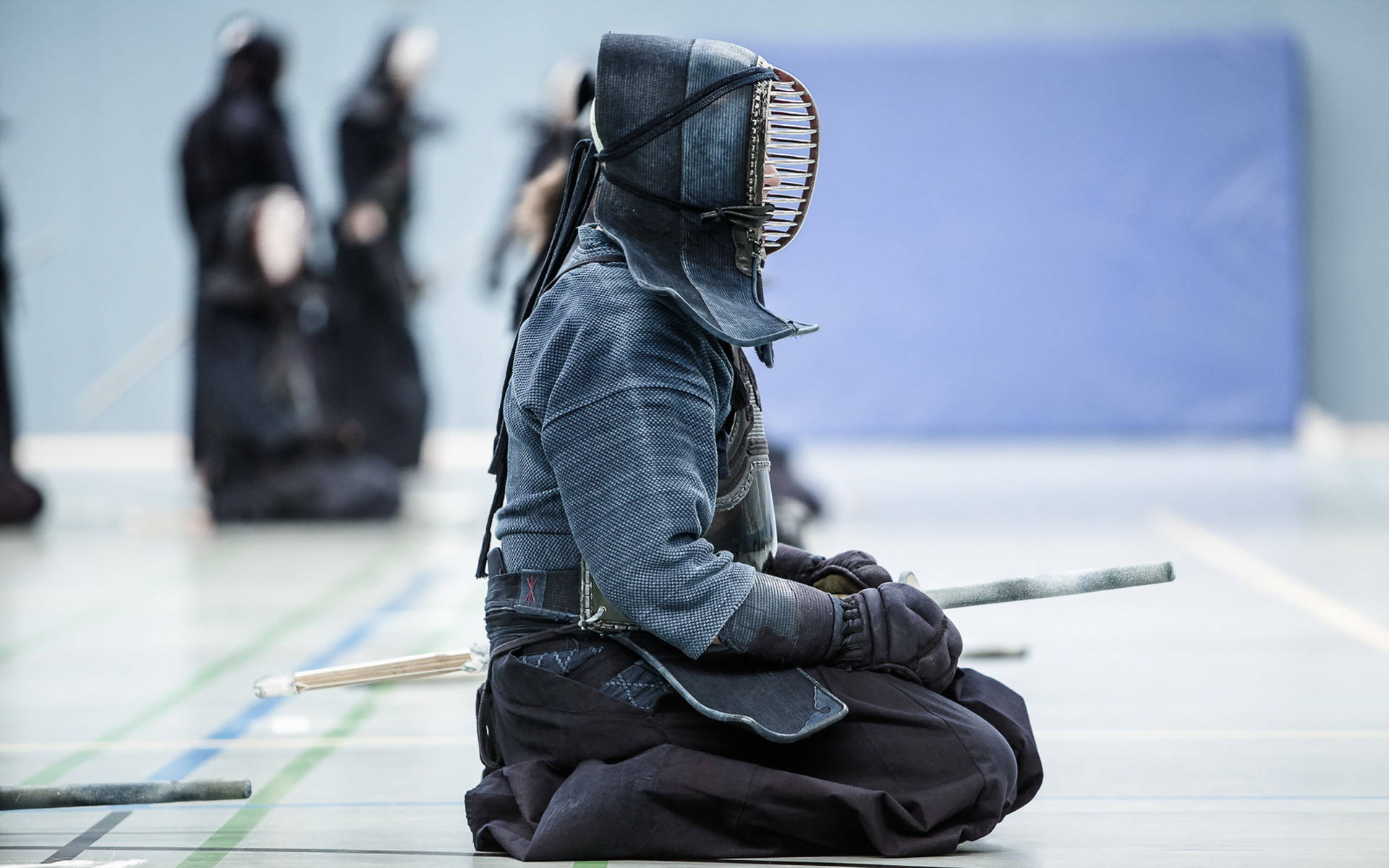 martial arts 桌布 壁紙 — 一名身穿全套防護裝備的劍士跪在道場地板上，手持竹劍，背景有模糊的對手。