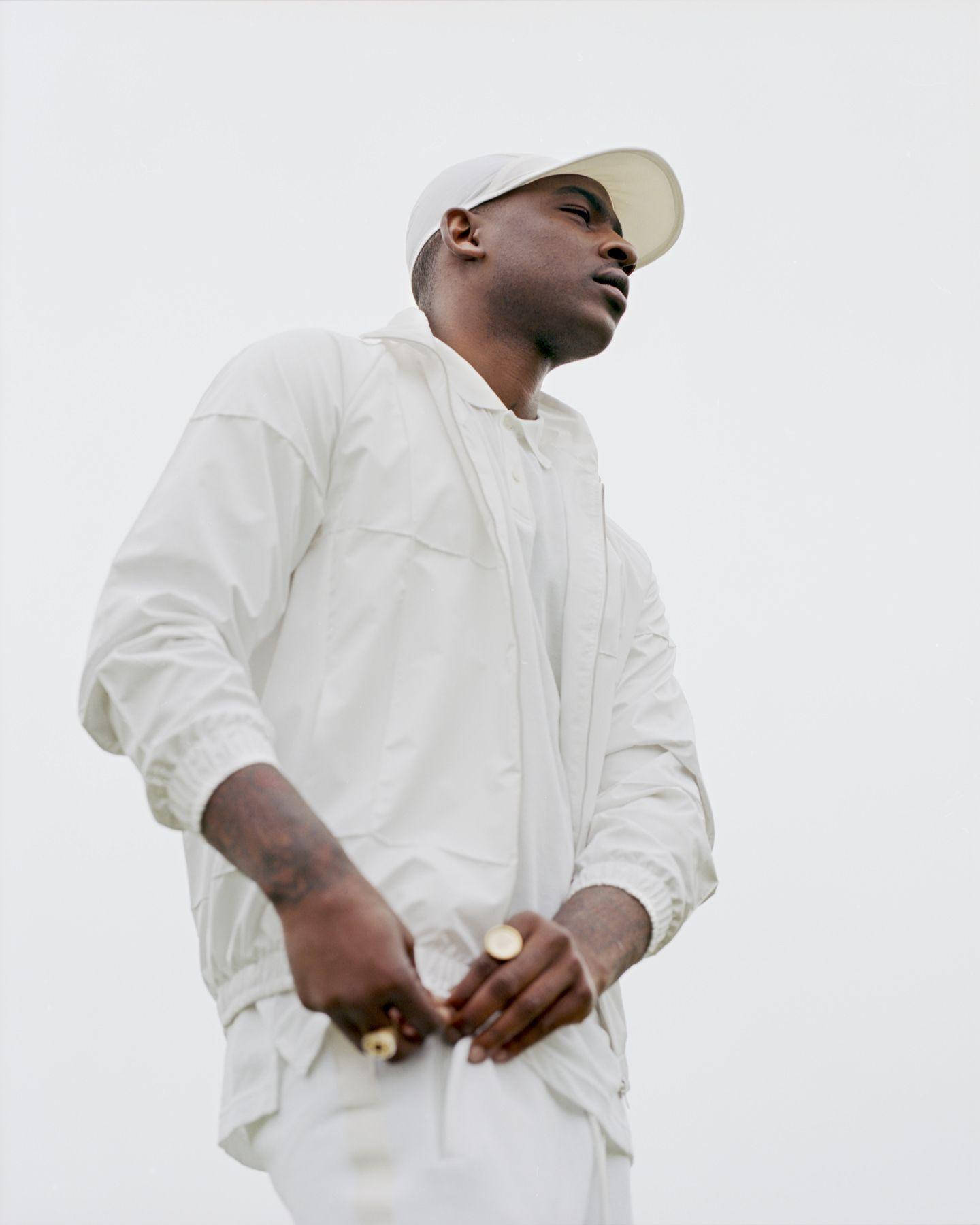 Skepta 桌布 壁紙 — 一名身穿全白服裝和帽子的男子，站在純白色背景前，表情若有所思。