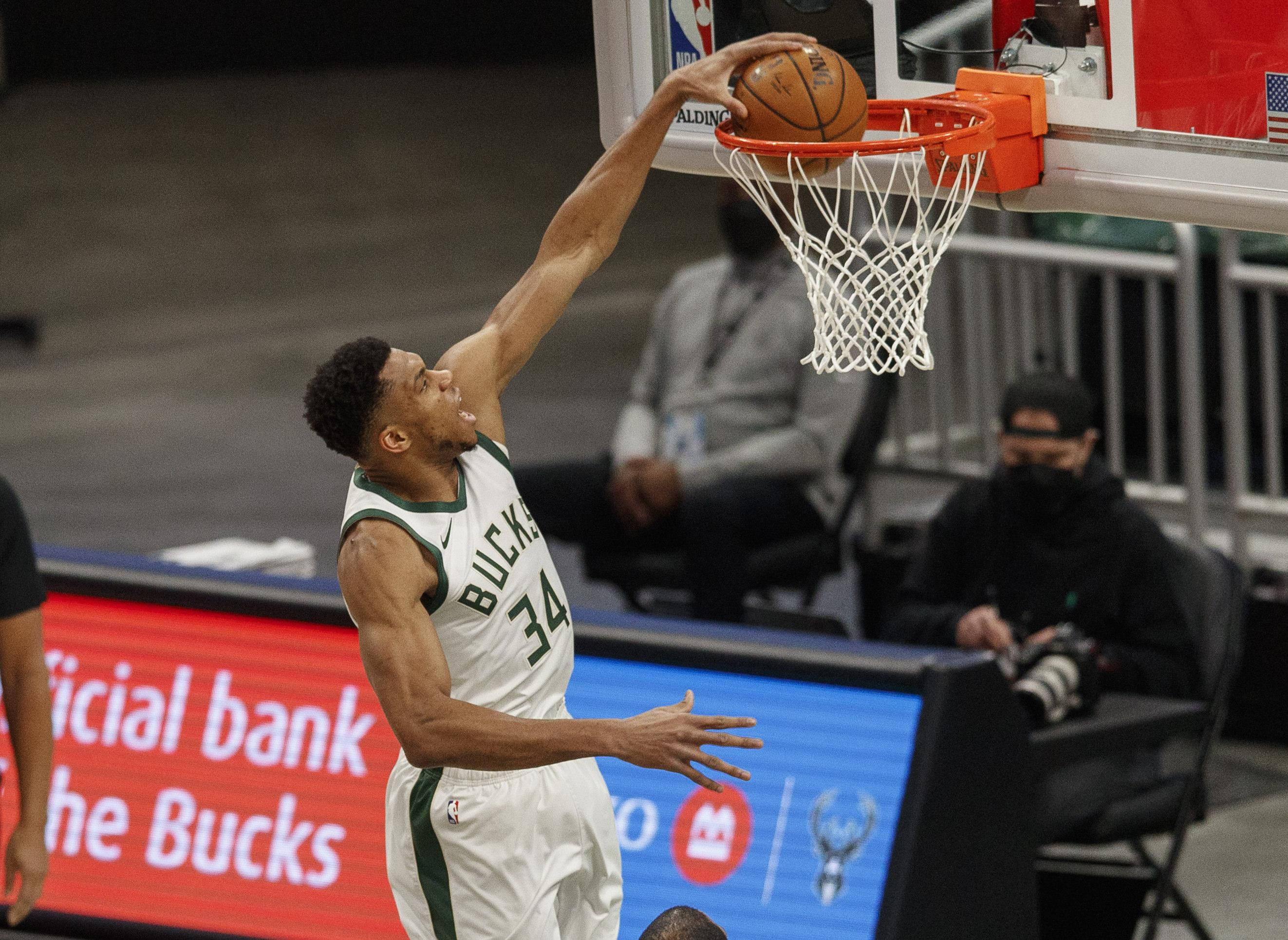 Giannis 桌布 壁紙 — 一名身穿公鹿隊球衣的籃球運動員在明亮的場館燈光下，於比賽中專注地灌籃。