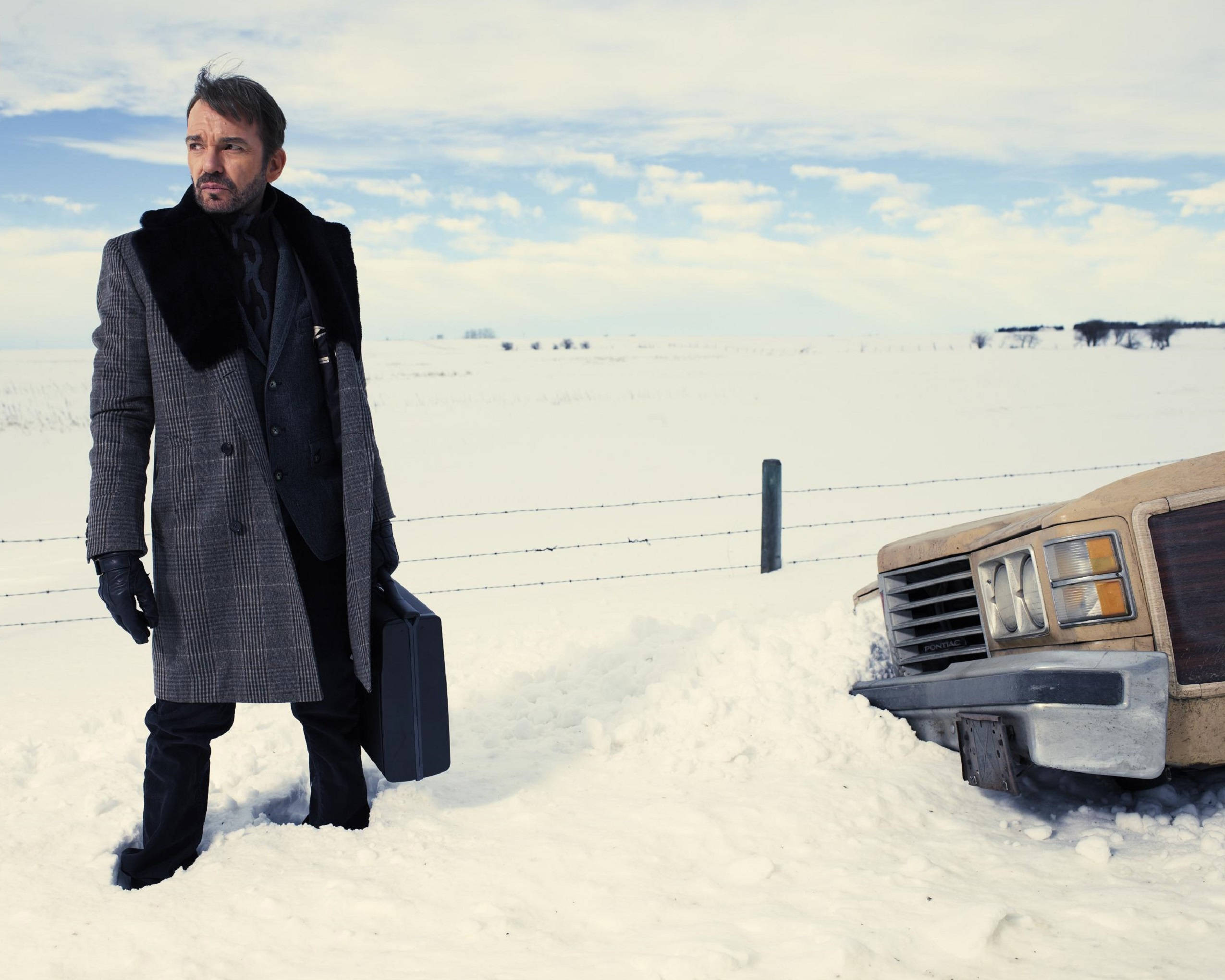 actor 桌布 壁紙 — 一名身穿冬季外套的男子站在一輛積雪的復古汽車旁，背景是廣闊的冰凍田野和陰天。