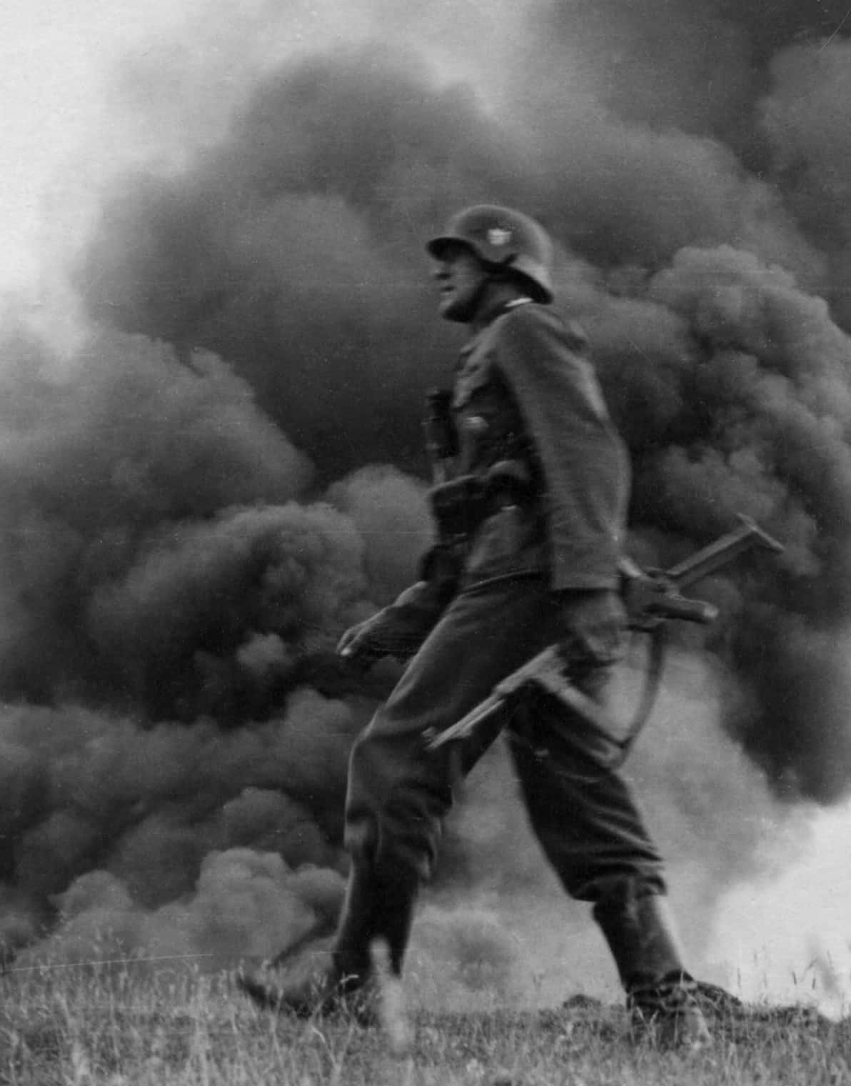 Ww2 iPhone 桌布 壁紙 — 一名身穿制服和頭盔的士兵在草叢田野上穿過滾滾濃煙向前邁進。
