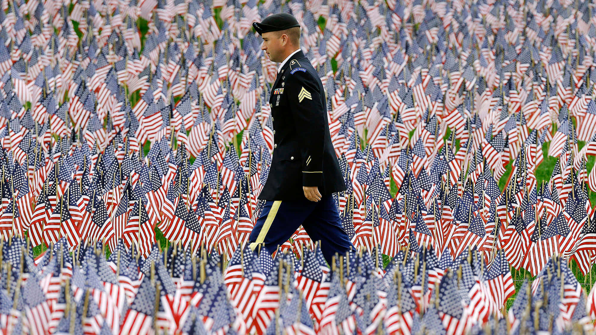 Memorial Day 桌布 壁紙 — 一名身穿制服的士兵在紀念場地莊嚴地走過廣闊的美國國旗田野。