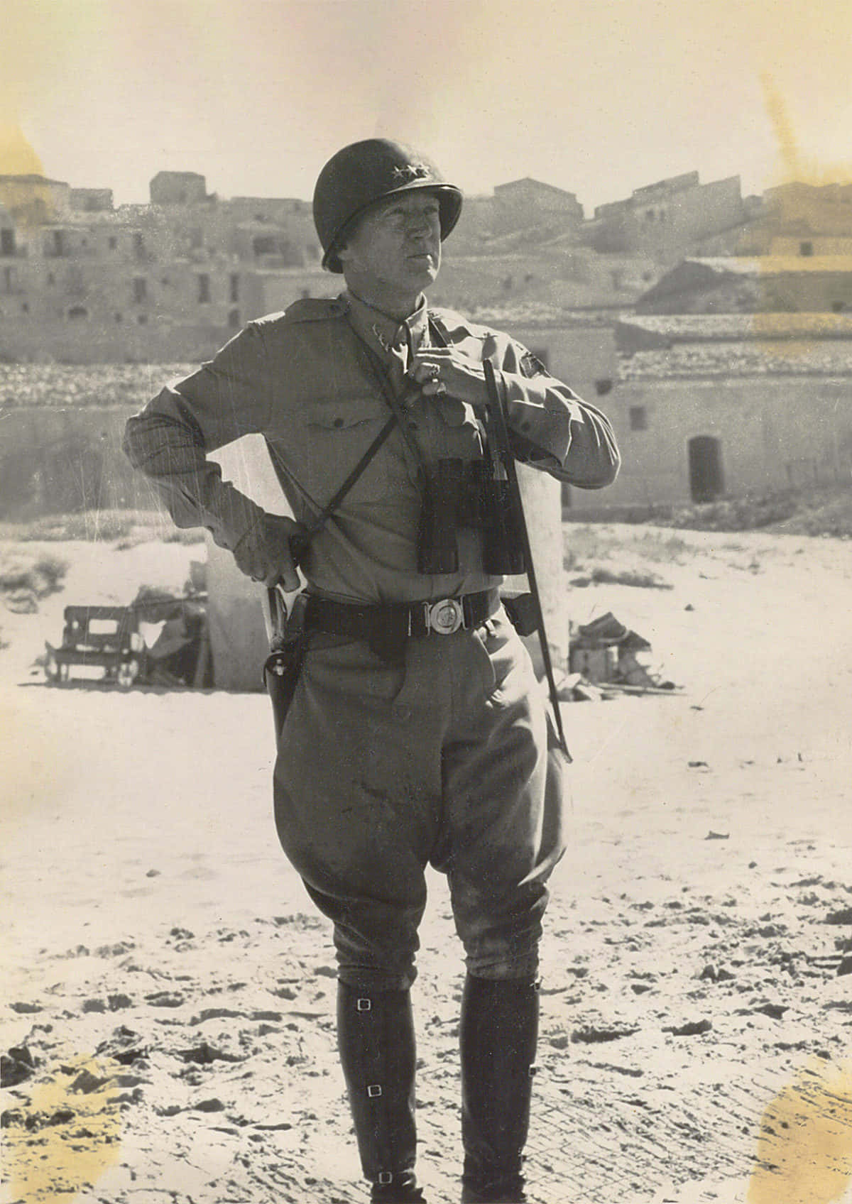 Ww2 桌布 壁紙 — 一名身穿制服的士兵在陽光明媚的沙漠小鎮中保持警覺，身後是風化的建築物。
