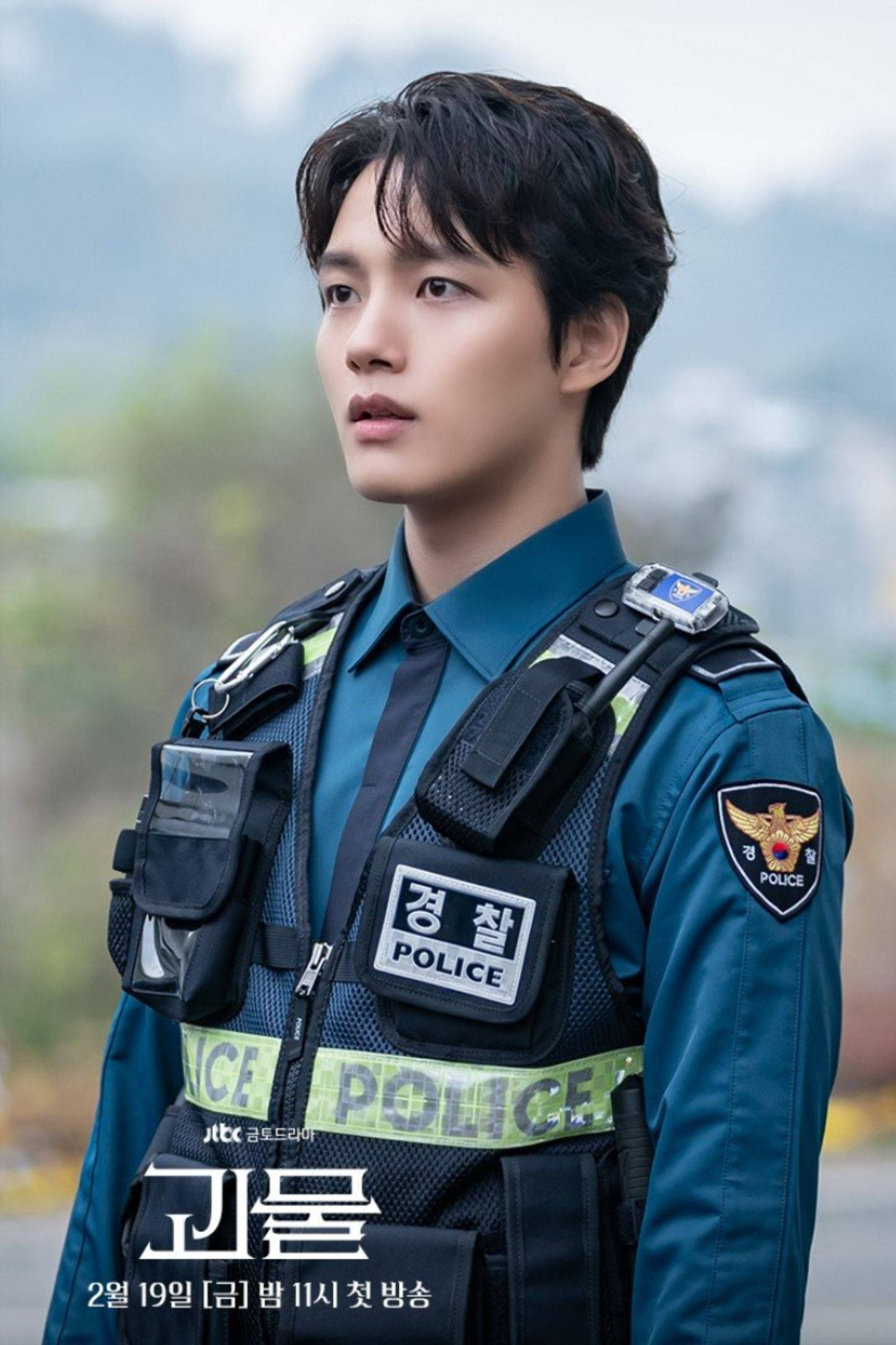 Jin 桌布 壁紙 — 一名身穿制服的年輕韓國警察在戶外若有所思地凝視著，背景是煙霧繚繞的山巒。