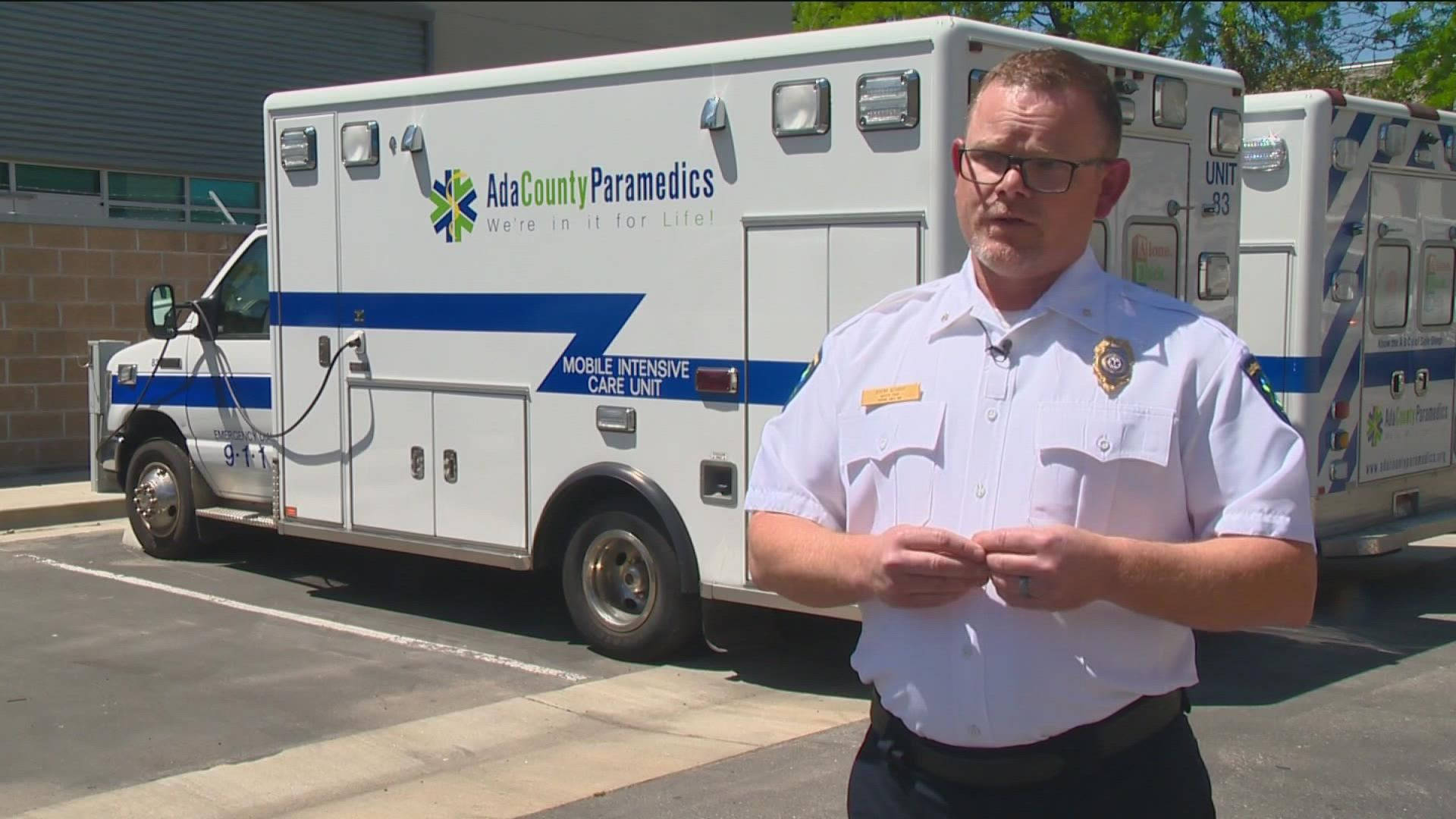 job 桌布 壁紙 — 一名身穿制服的醫護人員站在一輛白色的Ada County Paramedics救護車前，救護車停放在陽光明媚的空地上。