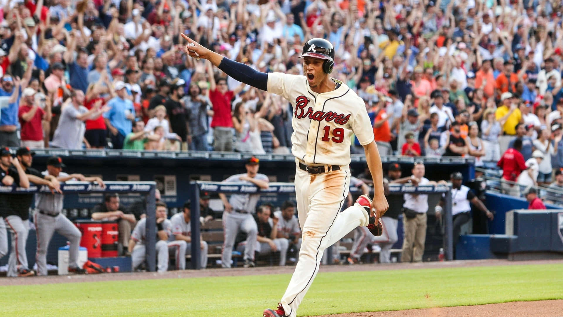 Atlanta Braves Desktop 桌布 壁紙 — 一名身穿勇士隊球衣的棒球運動員在陽光明媚的球場上勝利慶祝，背景是歡呼的人群。