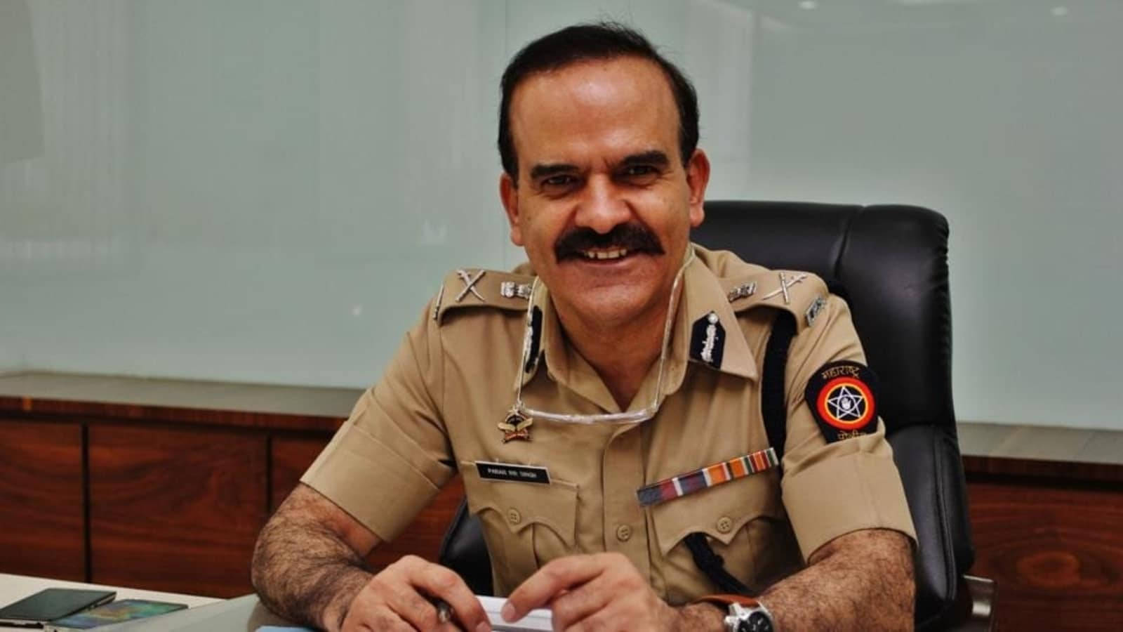Indian 桌布 壁紙 — 一名身穿卡其色制服、面帶微笑的警察坐在辦公室桌前，身後有木櫃和白色板。