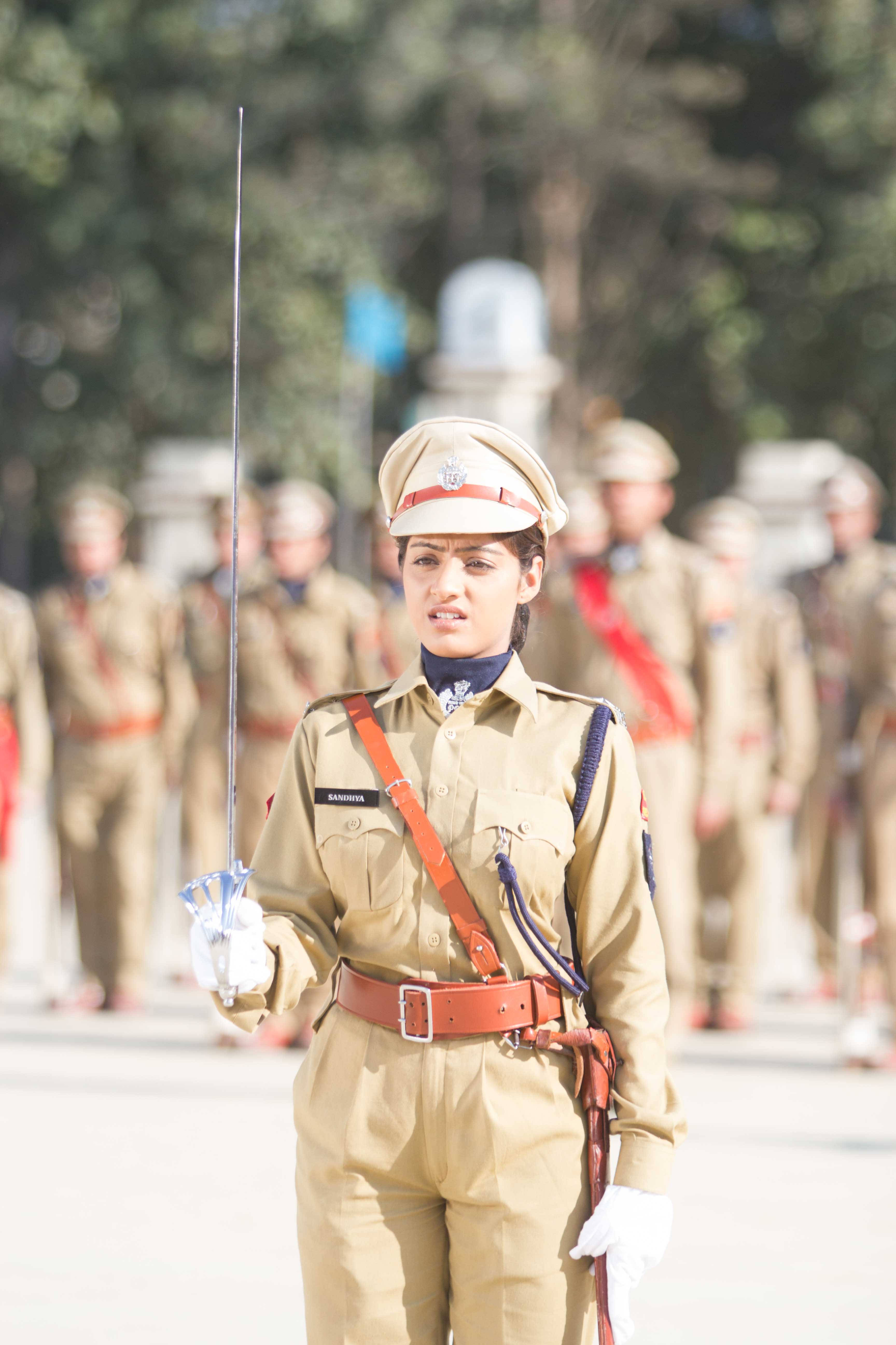 Indian 桌布 壁紙 — 一名身穿卡其色制服的女兵在戶外持劍立正，背景有其他士兵模糊不清。