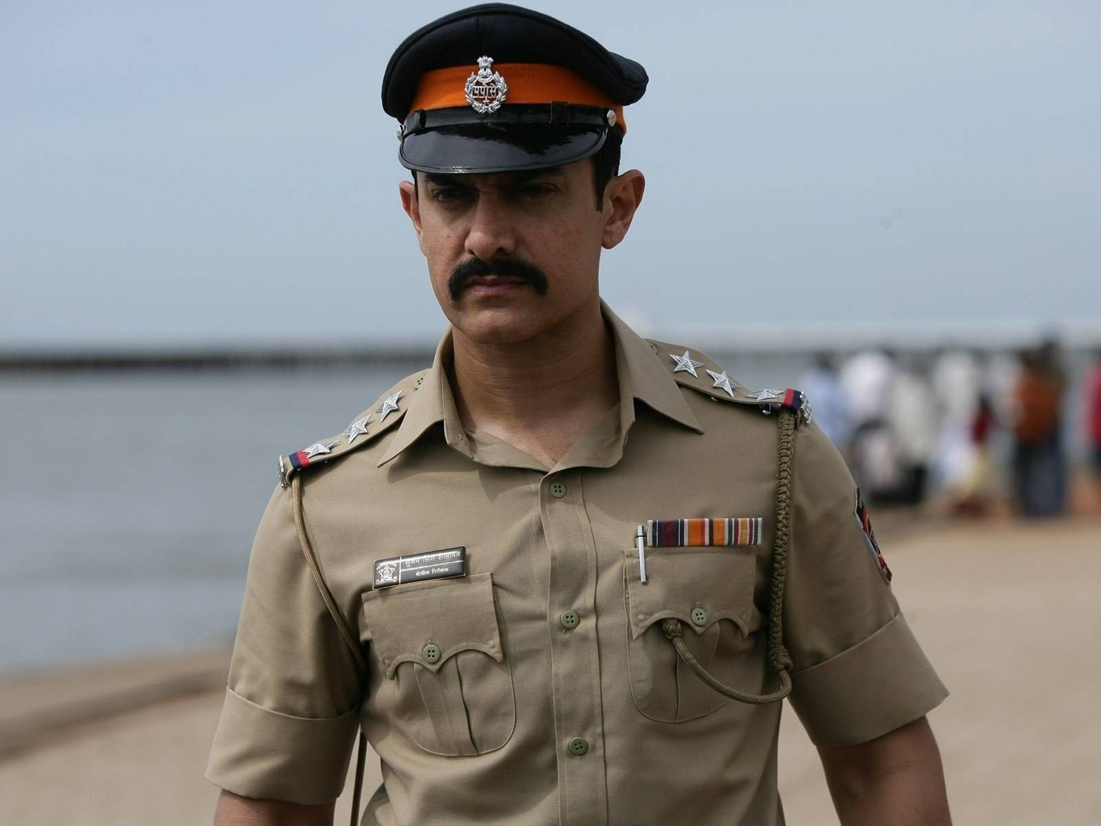 Indian 桌布 壁紙 — 一名身穿卡其色警察制服、佩戴星章和勳章的男子，在陰天下的海濱莊嚴地站立。