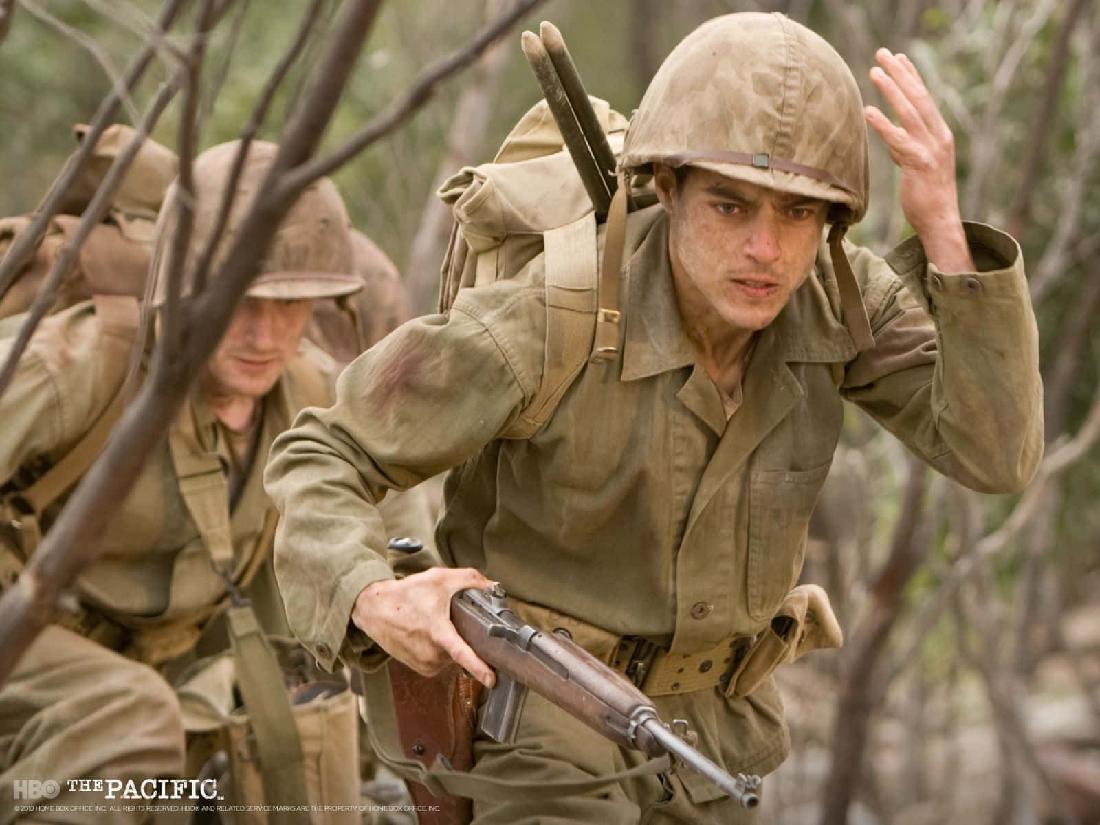 Marines 桌布 壁紙 — 一名身穿卡其色軍服和頭盔的士兵，手持步槍，全神貫注地穿過茂密的灌木叢。