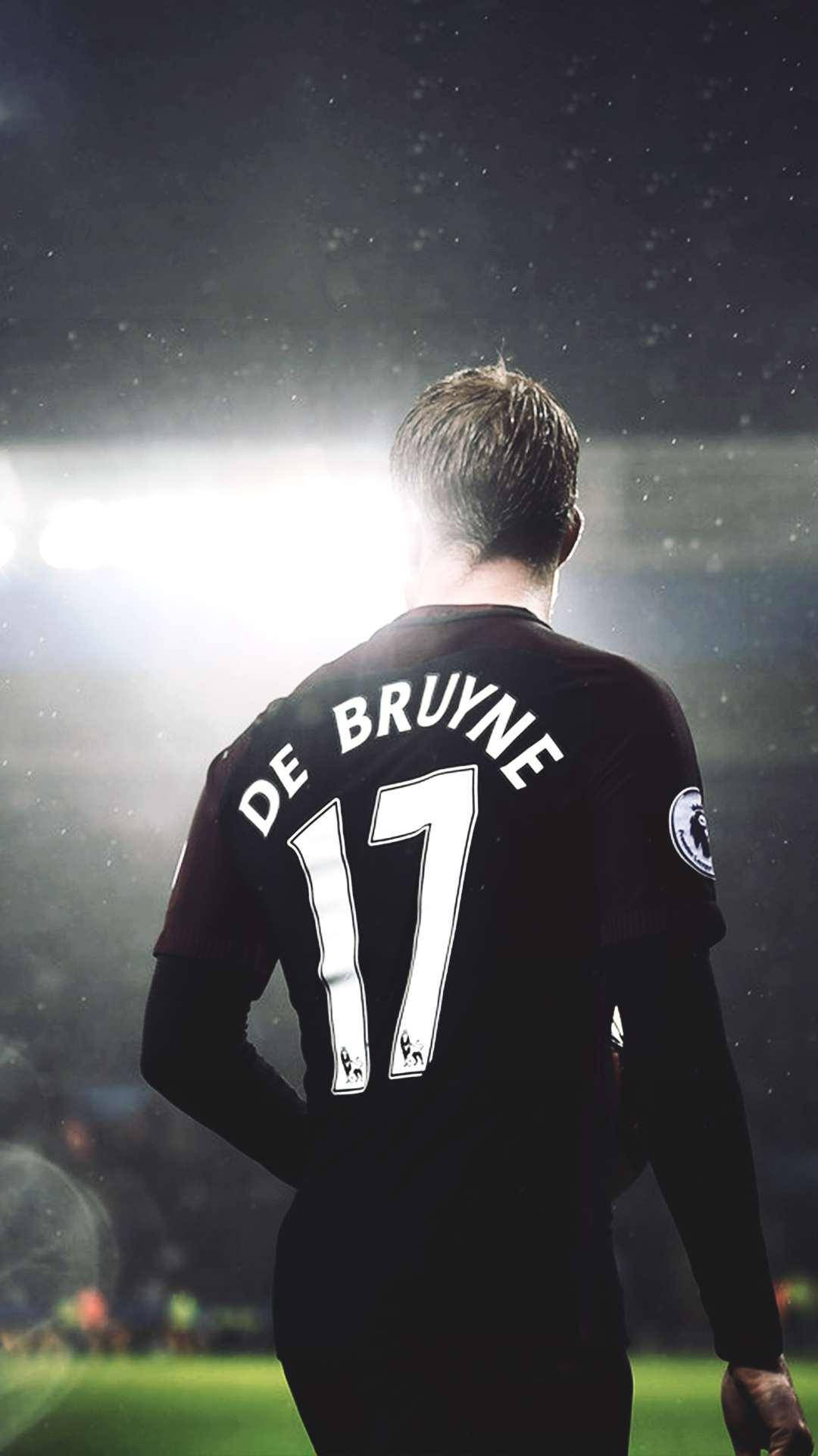 凱文·德布勞內 桌布 壁紙 — 一名身穿印有「DE BRUYNE 17」黑色球衣的足球員，在雨夜比賽中背對鏡頭站在球場燈光下。