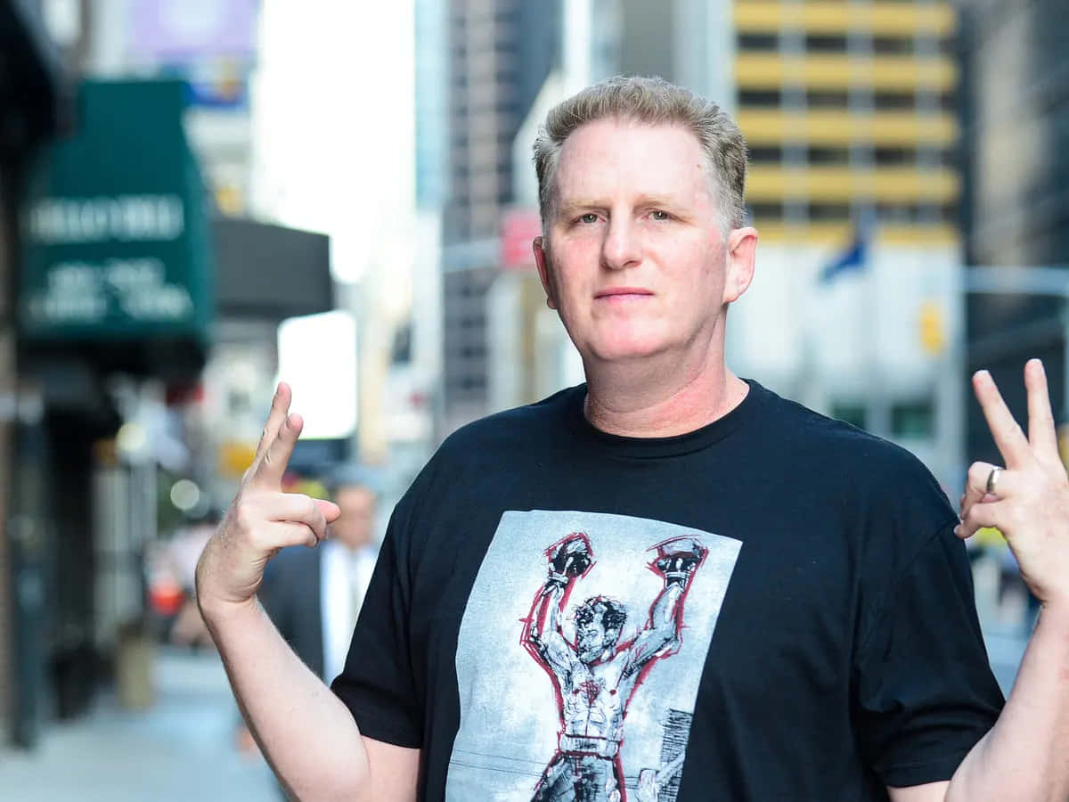 Michael Rapaport 桌布 壁紙 — 一名身穿印有Rocky圖案黑色T恤的男子，在繁忙的城市人行道上比出和平手勢。