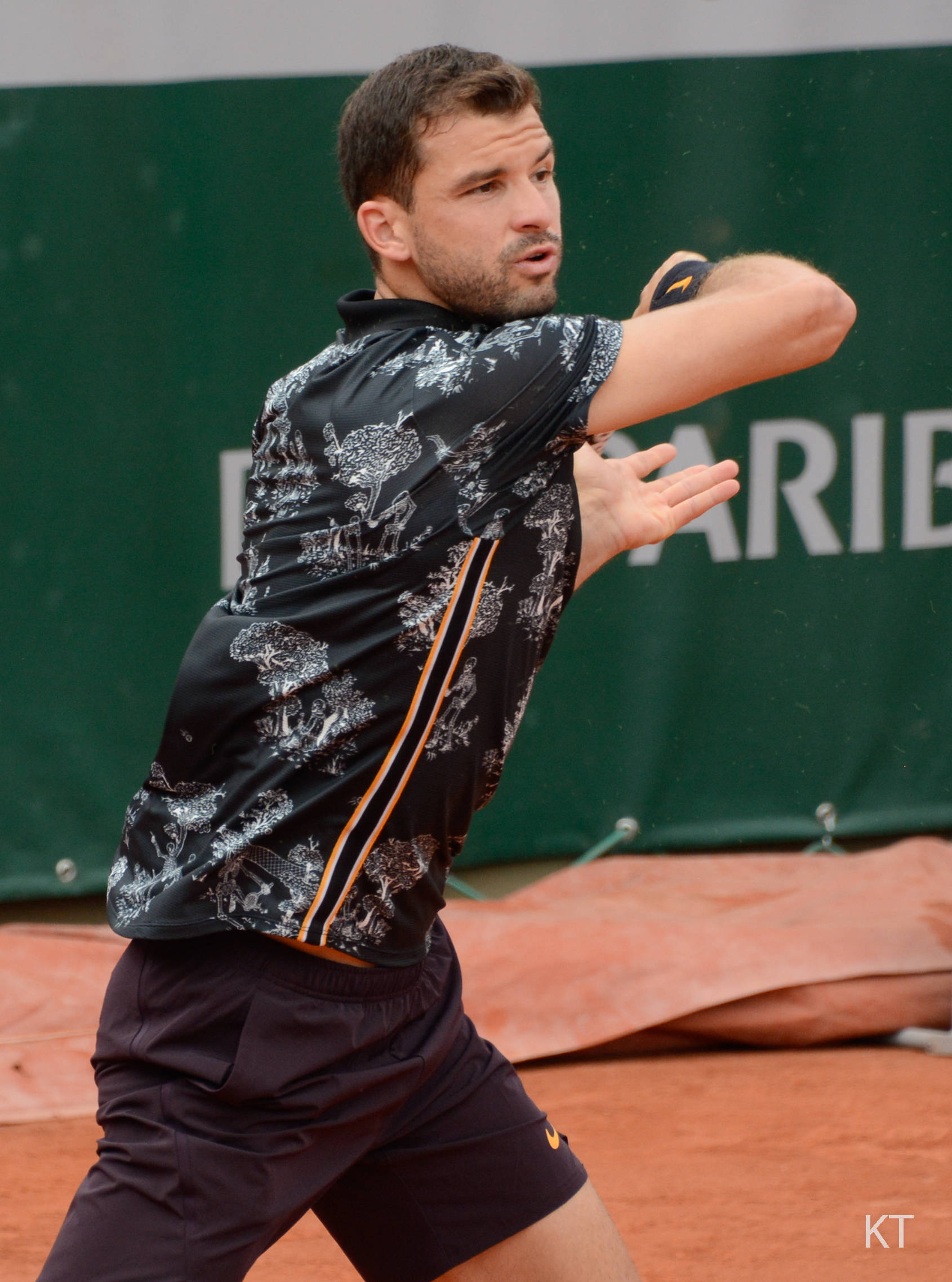 Tennis 桌布 壁紙 — 一名身穿圖案襯衫的男網球運動員在紅土場上揮拍，神情專注。