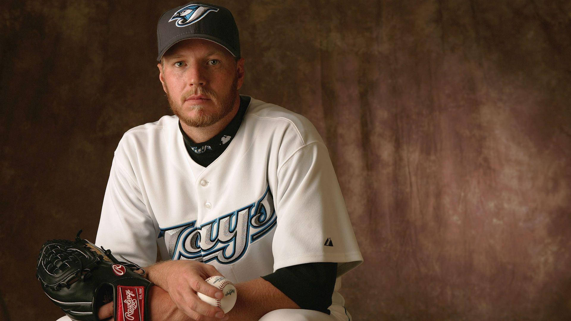 roy halladay 桌布 壁紙 — 一名身穿坦帕灣光芒隊球衣的棒球運動員，坐在有紋理的棕色背景前，手持手套和球。