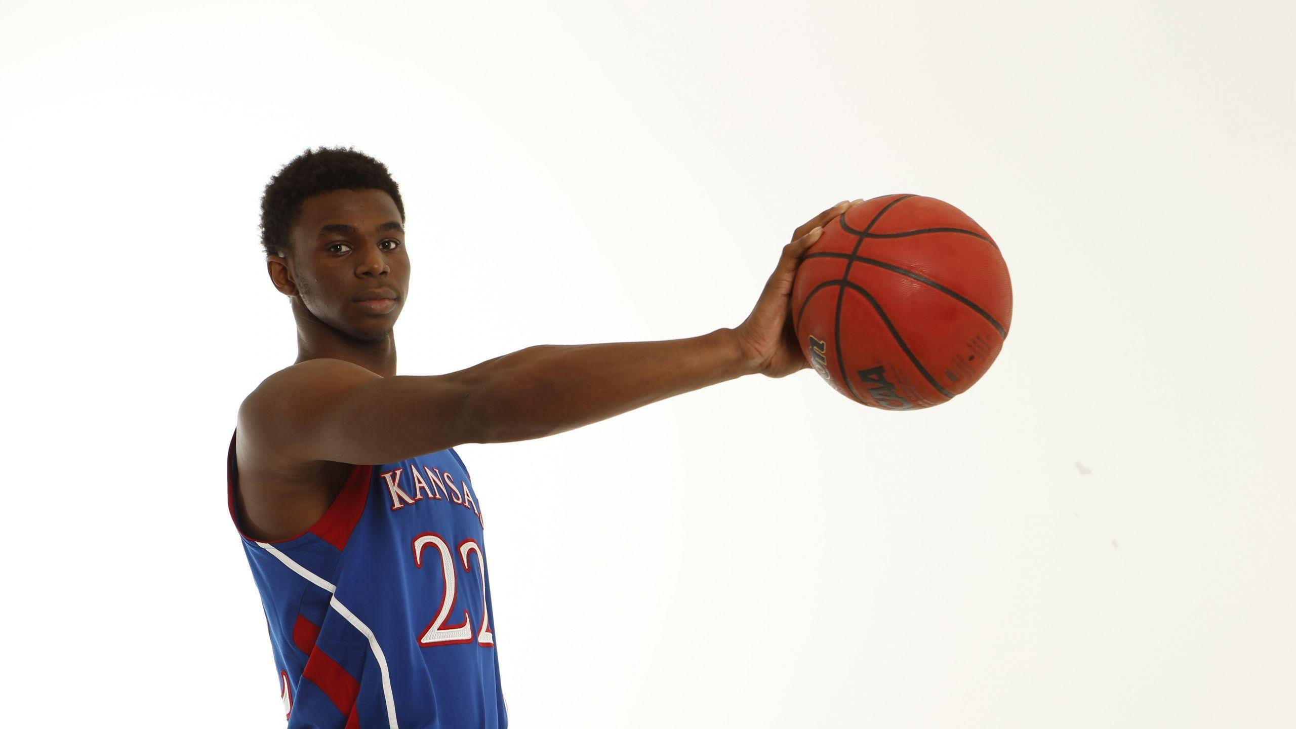 Andrew Wiggins 桌布 壁紙 — 一名身穿堪薩斯球衣的年輕籃球運動員，手持紅色籃球，準備在純白背景前投籃。