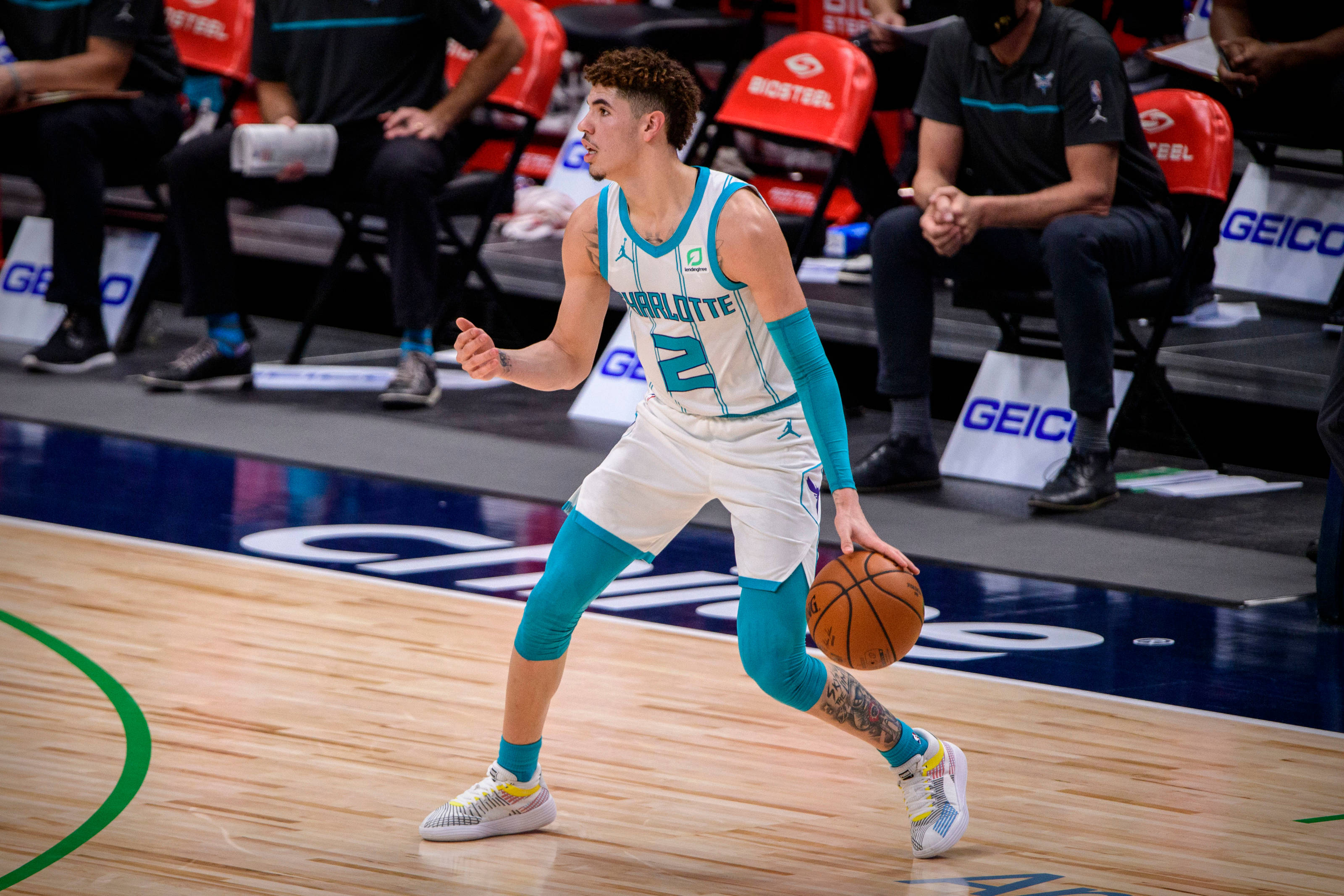 ball 桌布 壁紙 — 一名身穿夏洛特球衣的籃球運動員在拋光球場上運球，背景有隊友和教練。