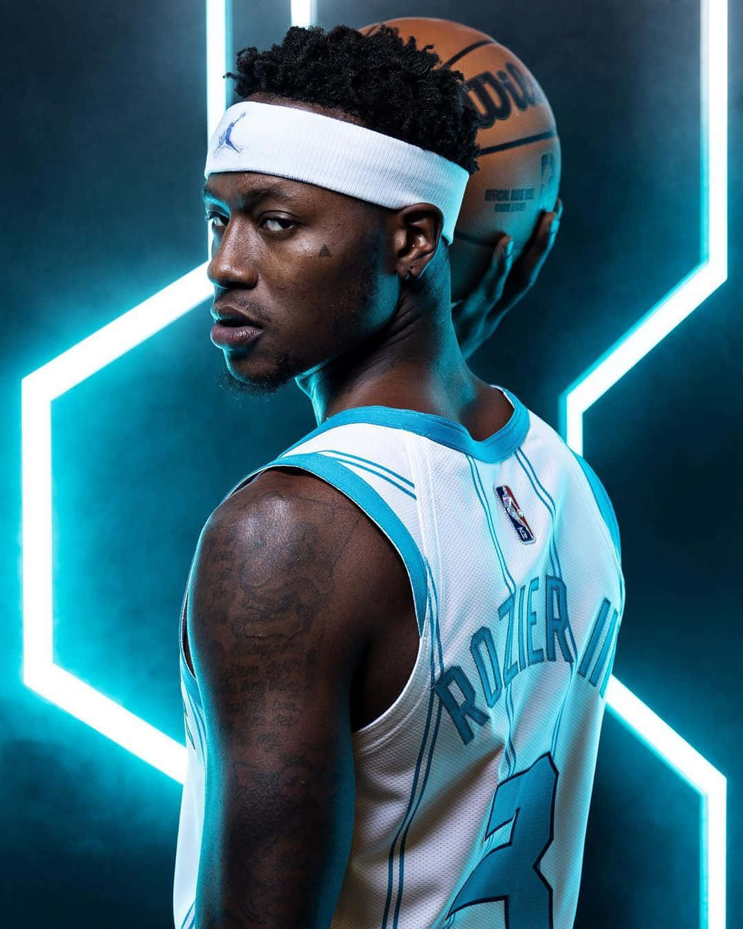 NBA 桌布 壁紙 — 一名身穿夏洛特黃蜂隊球衣的籃球運動員在黑暗的攝影棚中，手持籃球，背景是發光的霓虹六邊形。