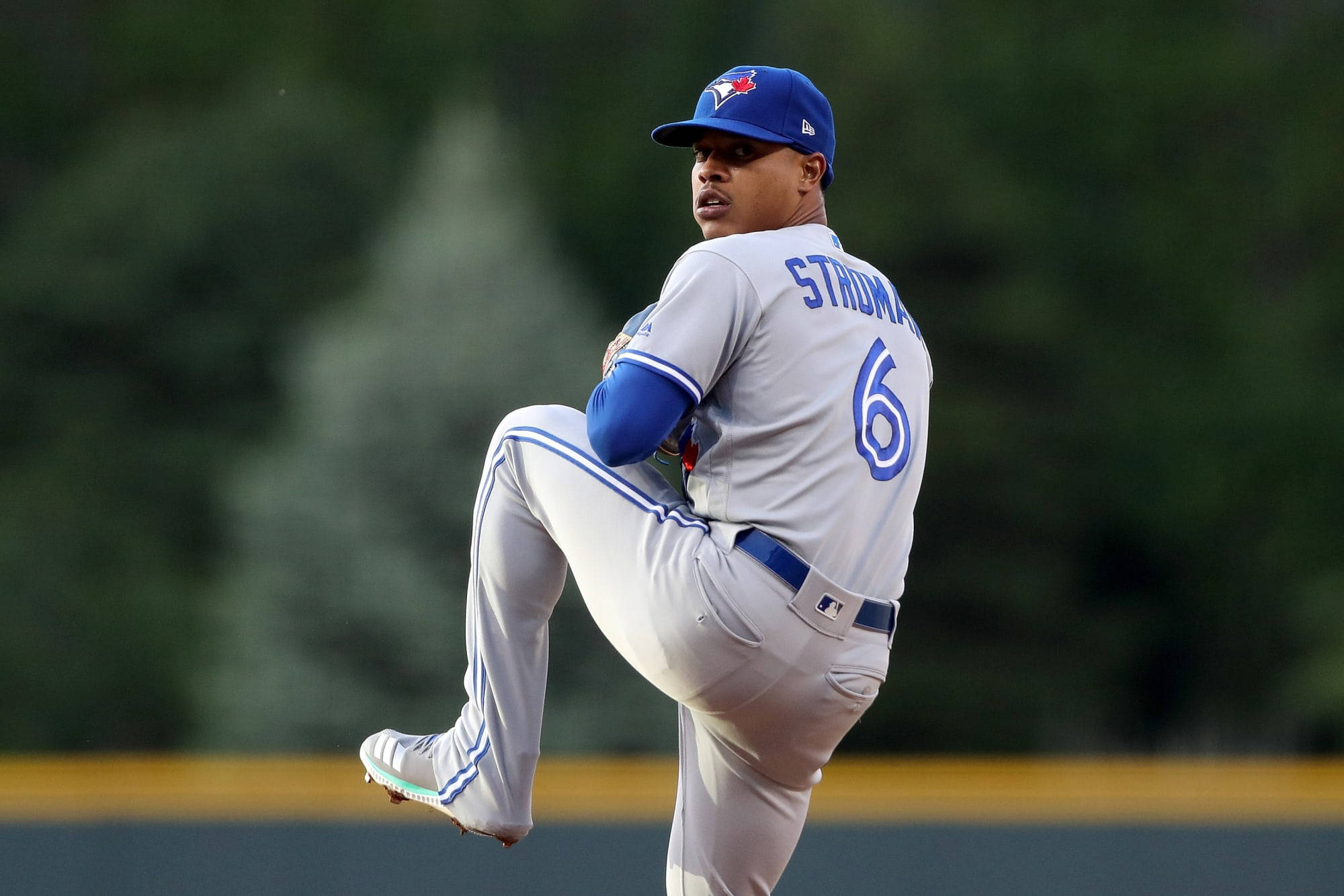 Marcus Stroman 桌布 壁紙 — 一名身穿多倫多藍鳥隊制服的棒球投手，在模糊的綠色球場背景下，集中精神用力投球。
