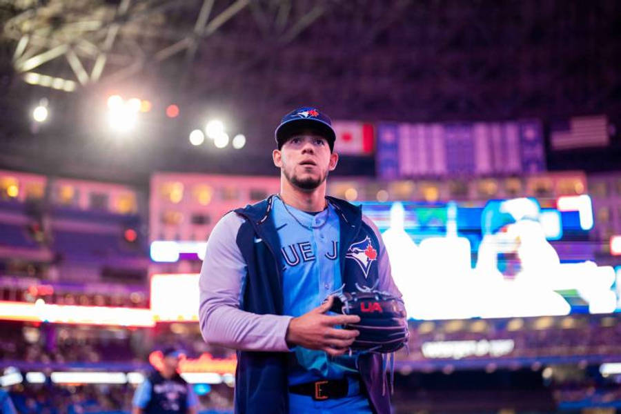 運動 桌布 壁紙 — 一名身穿多倫多藍鳥隊球衣的棒球選手，在夜晚燈光明亮的球場上莊嚴地站著，手持手套。